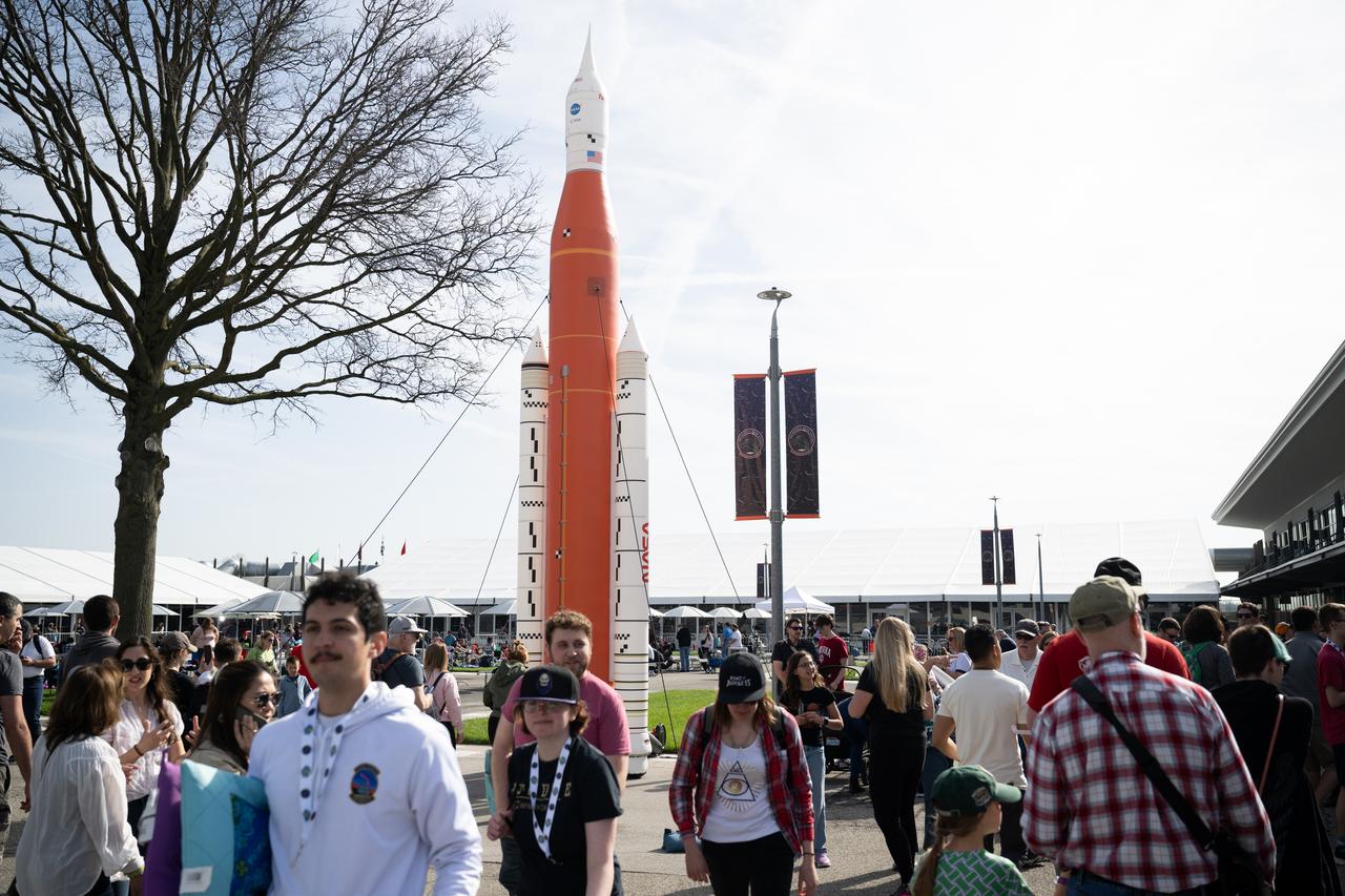 Attendees at the Indianapolis Motor Speedway walk past an inflatable version of NASA’s Space Launch System rocket ahead of the total solar eclipse, Monday, April 8, 2024, in Indianapolis, Ind. A total solar eclipse swept across a narrow portion of the North American continent from Mexico’s Pacific coast to the Atlantic coast of Newfoundland, Canada. A partial solar eclipse was visible across the entire North American continent along with parts of Central America and Europe.  Photo Credit: (NASA/Joel Kowsky)