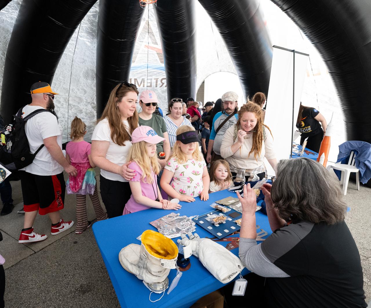 Attendees at the Indianapolis Motor Speedway view NASA exhibits ahead of the total solar eclipse, Monday, April 8, 2024, in Indianapolis, Ind. A total solar eclipse swept across a narrow portion of the North American continent from Mexico’s Pacific coast to the Atlantic coast of Newfoundland, Canada. A partial solar eclipse was visible across the entire North American continent along with parts of Central America and Europe.  Photo Credit: (NASA/Joel Kowsky)