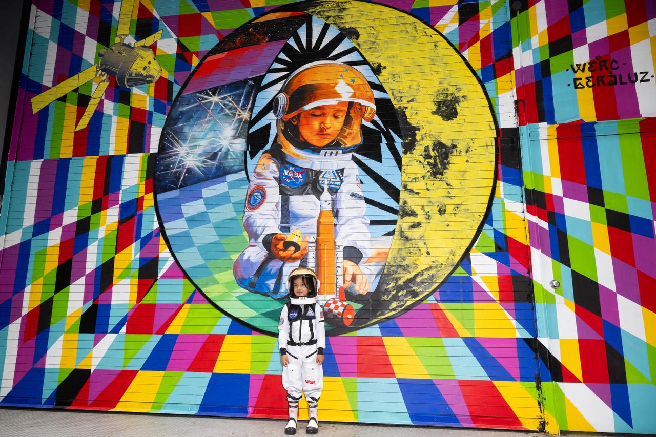 Amaru Alvarez, 5, the son of the artist team Geraluz and WERC and model for the mural, poses for picture with the mural “To the Moon, and Back” by the New York-based artist team that was created as part of the reimagined NASA Art Program, Tuesday, September 24, 2024, at 350 Hudson Street in New York City. The murals use geometrical patterns to invite deeper reflection on the exploration, creativity, and connection with the cosmos.  Photo Credit: (NASA/Joel Kowsky)