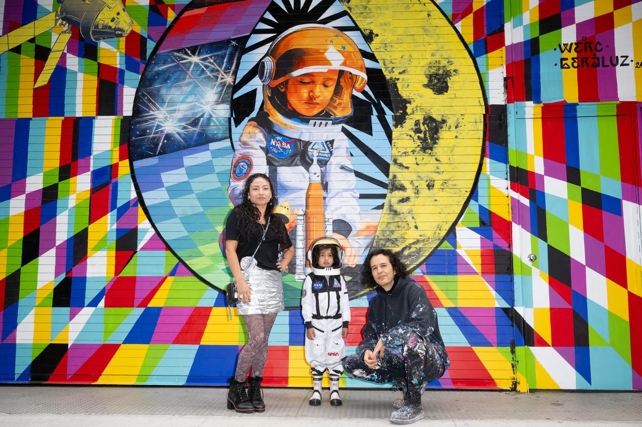 The New York-based artist team Geraluz, left, and WERC, right, and their son Amaru Alvarez, 5, pose for picture with the mural “To the Moon, and Back” by the artist team that was created as part of the reimagined NASA Art Program, Tuesday, September 24, 2024, at 350 Hudson Street in New York City. The murals use geometrical patterns to invite deeper reflection on the exploration, creativity, and connection with the cosmos. Photo Credit: (NASA/Joel Kowsky)