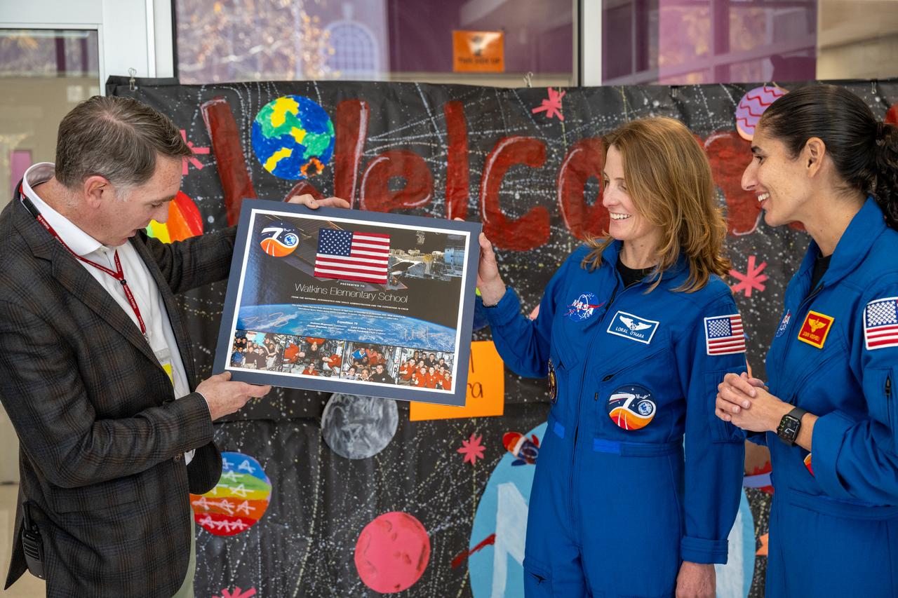 NASA astronauts Loral O’Hara, second from right, and Jasmin Moghbeli, right, present a montage to Principal MScott Berkowitz prior to an engagement event at Catherine Watkins Elementary School Monday, Dec. 2, 2024 in Washington. O’Hara and Moghbeli spent six months in space as part of Expedition 70 aboard the International Space Station. Photo Credit: (NASA/Keegan Barber)