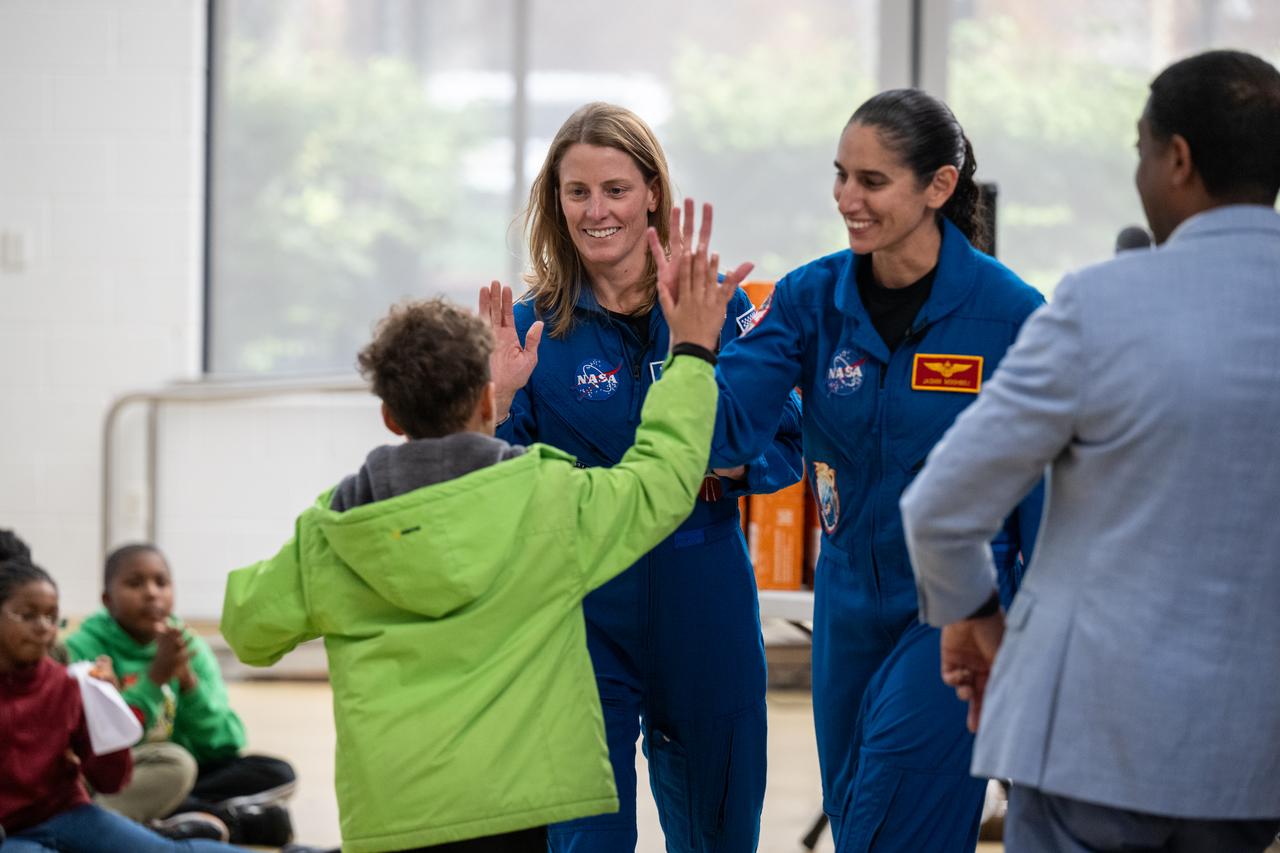 NASA astronauts Loral O’Hara and Jasmin Moghbeli, seen in blue flight suits, high five a student during an engagement event at Catherine Watkins Elementary School Monday, Dec. 2, 2024 in Washington. O’Hara and Moghbeli spent six months in space as part of Expedition 70 aboard the International Space Station. Photo Credit: (NASA/Keegan Barber)
