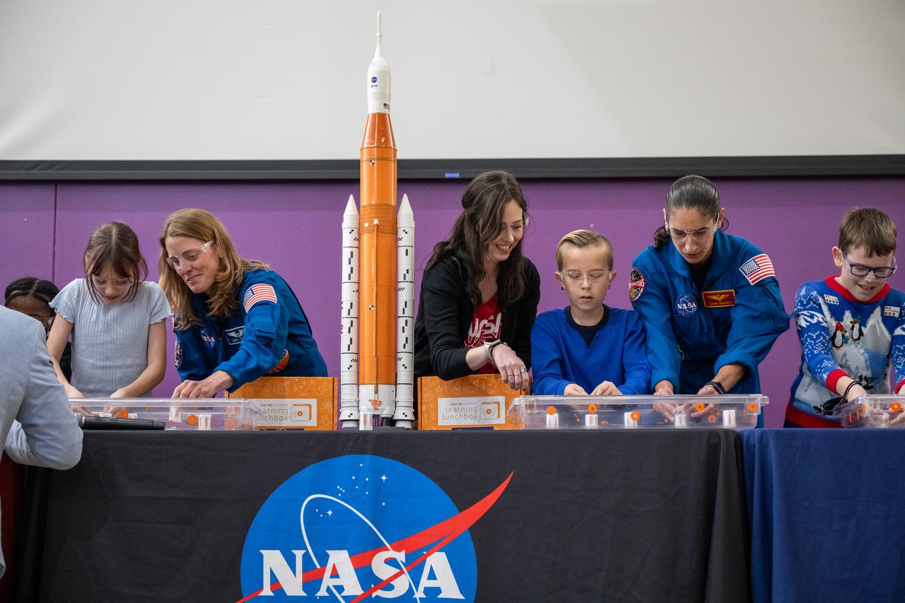 NASA astronauts Loral O’Hara and Jasmin Moghbeli, seen in blue flight suits, are joined by NASA and COSI staff during science demonstrations with students at an engagement event at Catherine Watkins Elementary School Monday, Dec. 2, 2024 in Washington. O’Hara and Moghbeli spent six months in space as part of Expedition 70 aboard the International Space Station. Photo Credit: (NASA/Keegan Barber)