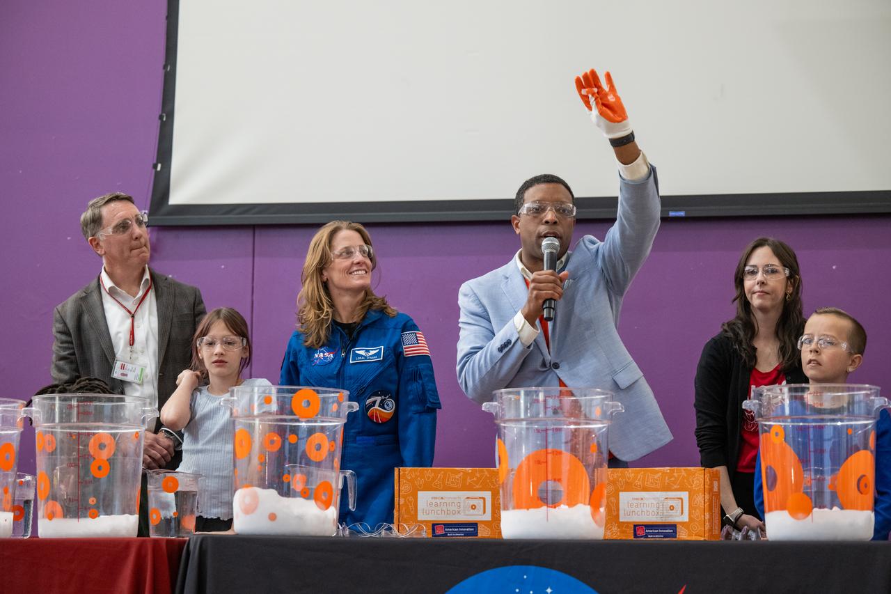 Center of Science and Industry (COSI) Chief Strategy Officer Stephen White, joined by Principal MScott Berkowitz, left, and NASA Astronaut Loral O’Hara, second from left, displays a piece of dry ice to students during a science demonstration at Catherine Watkins Elementary School Monday, Dec. 2, 2024 in Washington. O’Hara and Moghbeli spent six months in space as part of Expedition 70 aboard the International Space Station. Photo Credit: (NASA/Keegan Barber)