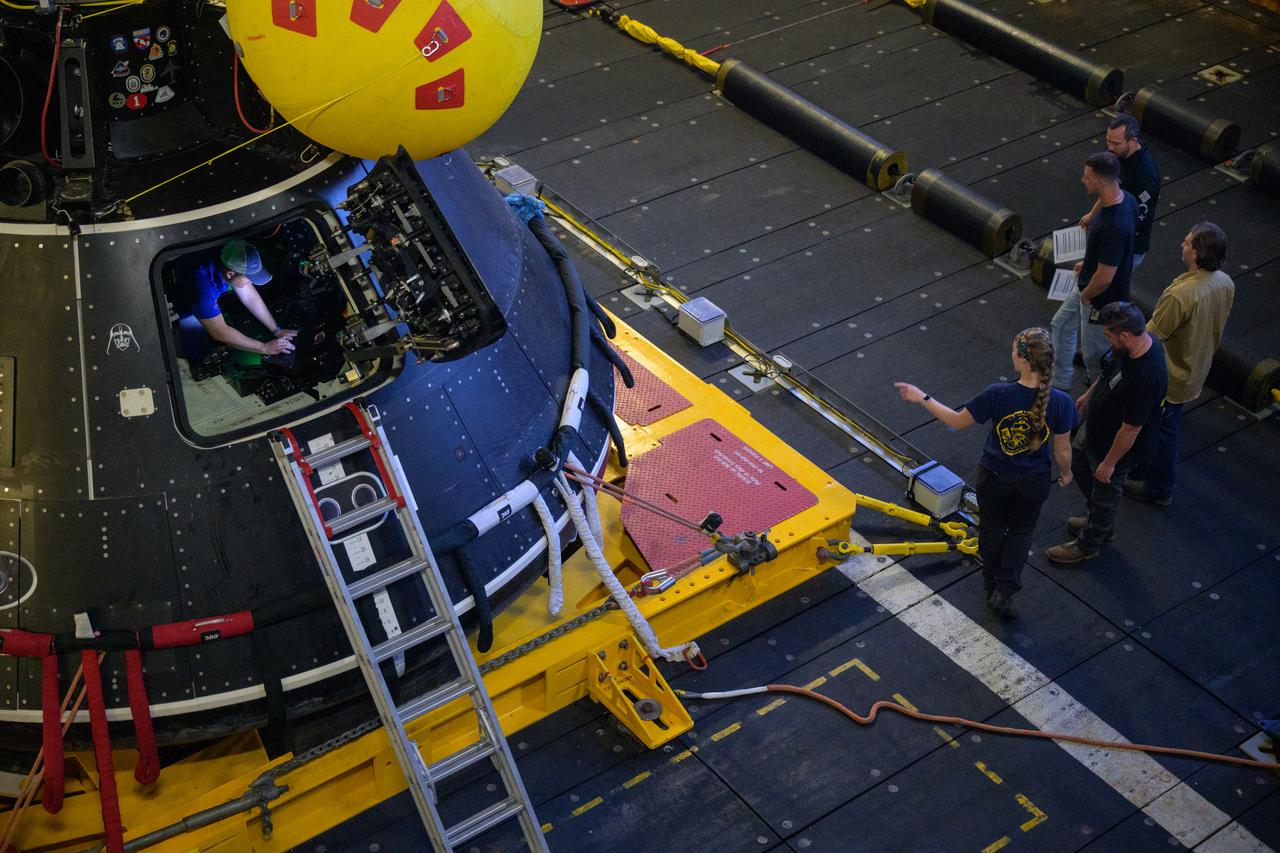 Teams work on the Crew Module Test Article (CMTA), a full scale mockup of the Orion spacecraft, as it sits sits nestled in its cradle during Underway Recovery Test-12 onboard USS Somerset off the coast of California, Wednesday, March 26, 2025. During the test, NASA and Department of Defense teams are practicing to ensure recovery procedures are validated as NASA plans to send Artemis II astronauts around the Moon and splashdown in the Pacific Ocean.  Photo Credit: (NASA/Joel Kowsky)