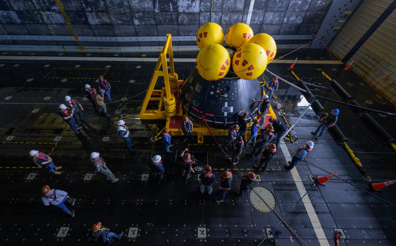 Teams work on the Crew Module Test Article (CMTA), a full scale mockup of the Orion spacecraft, as it sits sits nestled in its cradle during Underway Recovery Test-12 onboard USS Somerset off the coast of California, Wednesday, March 26, 2025. During the test, NASA and Department of Defense teams are practicing to ensure recovery procedures are validated as NASA plans to send Artemis II astronauts around the Moon and splashdown in the Pacific Ocean. Photo Credit: (NASA/Bill Ingalls)