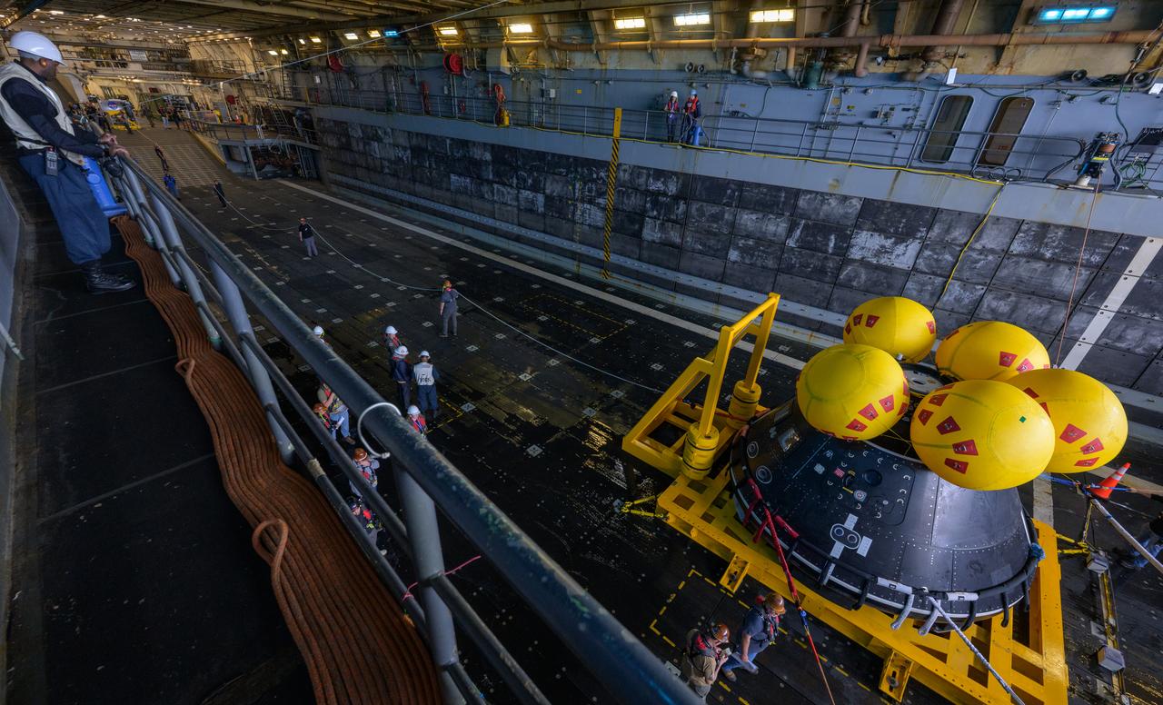 Teams work on the Crew Module Test Article (CMTA), a full scale mockup of the Orion spacecraft, as it sits sits nestled in its cradle during Underway Recovery Test-12 onboard USS Somerset off the coast of California, Wednesday, March 26, 2025. During the test, NASA and Department of Defense teams are practicing to ensure recovery procedures are validated as NASA plans to send Artemis II astronauts around the Moon and splashdown in the Pacific Ocean. Photo Credit: (NASA/Bill Ingalls)