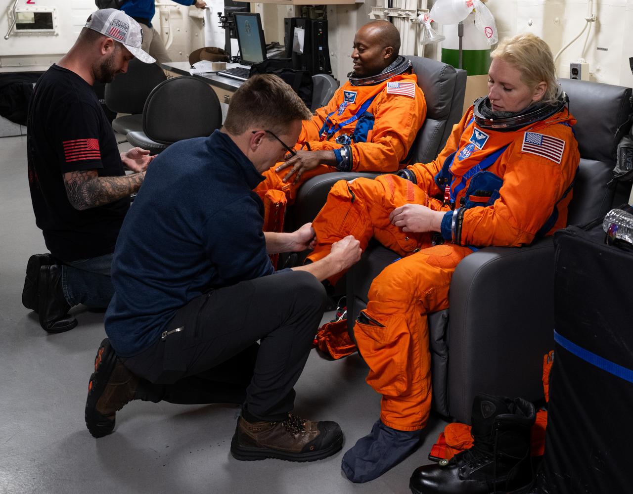 NASA astronauts Andre Douglas, left, and Deniz Burnham, are seen as they are assisted with putting on their Orion Crew Survival System suits as they prepare to take part in practicing Artemis recovery procedures during Underway Recovery Test-12 onboard USS Somerset, Thursday, March 27, 2025. During the test, NASA and Department of Defense teams are practicing to ensure recovery procedures are validated as NASA plans to send the Artemis II astronauts around the Moon and splashdown in the Pacific Ocean.  Photo Credit: (NASA/Joel Kowsky)