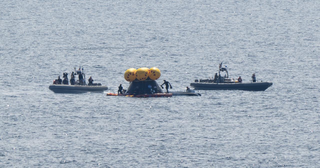 Teams work around the Crew Module Test Article (CMTA) as they practice Artemis recovery operations during Underway Recovery Test-12 onboard USS Somerset off the coast of California, Thursday, March 27, 2025. During the test, NASA and Department of Defense teams are practicing to ensure recovery procedures are validated as NASA plans to send the Artemis II astronauts around the Moon and splashdown in the Pacific Ocean. Photo Credit: (NASA/Joel Kowsky)