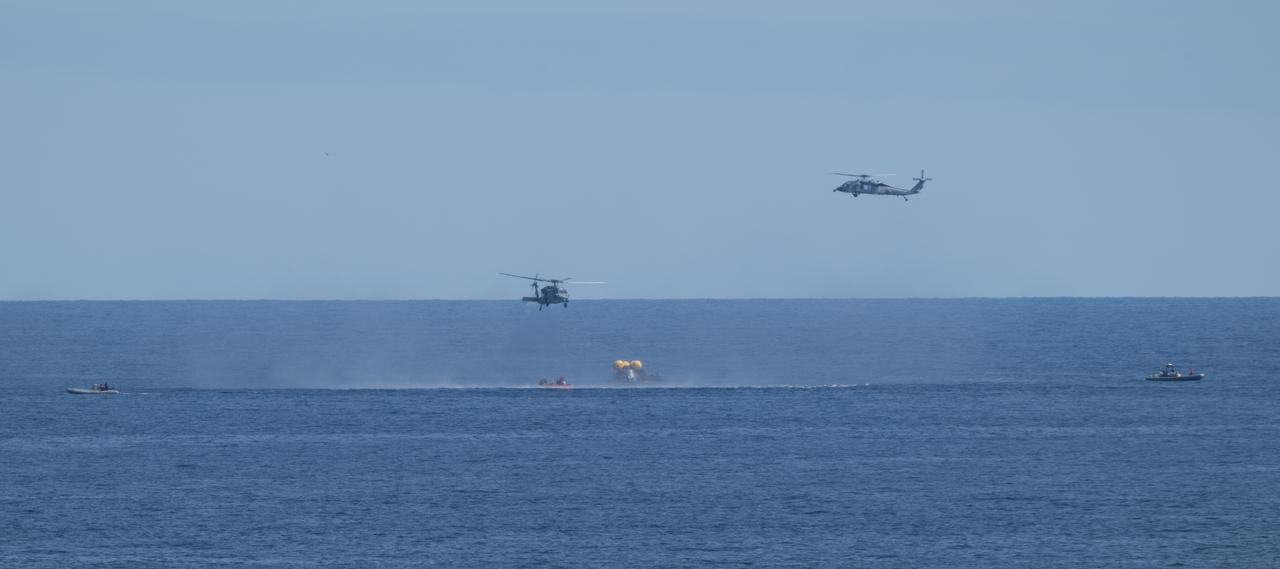 Two Navy MH-60 Seahawks from Helicopter Sea Combat Squadron (HSC) 23 are seen as they approach the Crew Module Test Article (CMTA) to recover crew members as NASA and Navy recovery teams practice operations during Underway Recovery Test-12 onboard USS Somerset, Thursday, March 27, 2025. During the test, NASA and Department of Defense teams are practicing to ensure recovery procedures are validated as NASA plans to send the Artemis II astronauts around the Moon and splashdown in the Pacific Ocean.  Photo Credit: (NASA/Joel Kowsky)