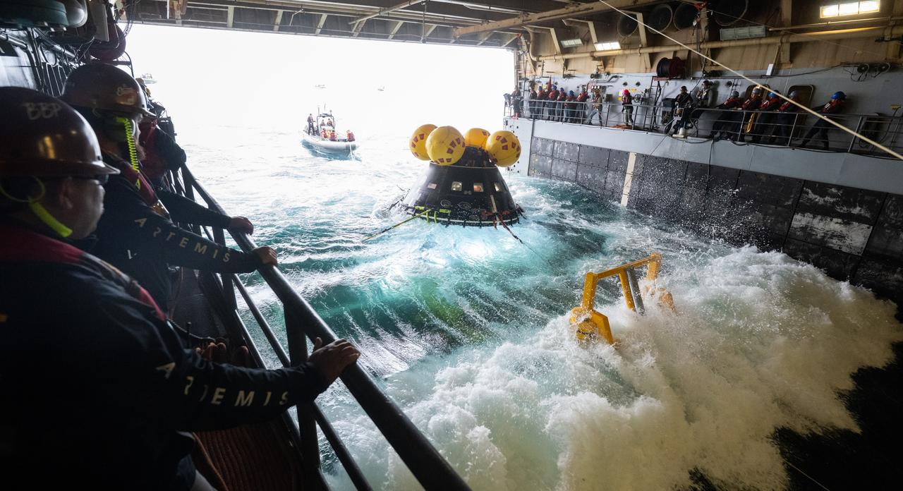A wave breaks inside the well deck of USS Somerset as teams work to recover the Crew Module Test Article (CMTA), a full scale replica of the Orion spacecraft, as they practice Artemis recovery operations during Underway Recovery Test-12 off the coast of California, Thursday, March 27, 2025. During the test, NASA and Department of Defense teams are practicing to ensure recovery procedures are validated as NASA plans to send the Artemis II astronauts around the Moon and splashdown in the Pacific Ocean.  Photo Credit: (NASA/Joel Kowsky)
