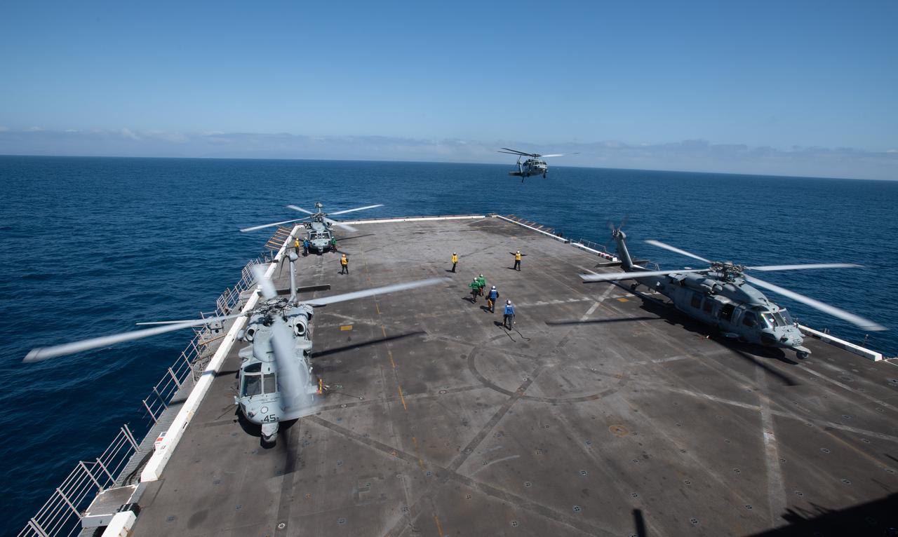 Three Navy MH-60 Seahawks from Helicopter Sea Combat Squadron (HSC) 23 are seen on the deck of USS Somerset as a fourth approaches to land as teams practice Artemis recovery operations during Underway Recovery Test-12 off the coast of California, Friday, March 28, 2025. During the test, NASA and Department of Defense teams are practicing to ensure recovery procedures are validated as NASA plans to send the Artemis II astronauts around the Moon and splashdown in the Pacific Ocean.  Photo Credit: (NASA/Bill Ingalls and Joel Kowsky)
