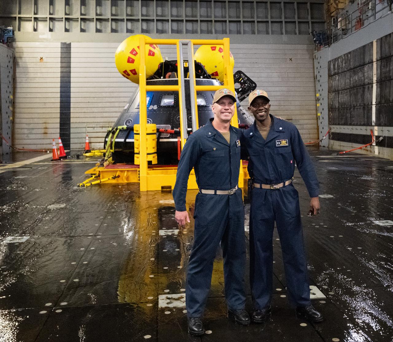Capt. Andrew Koy, commanding officer, and Cdr. Kevin Mutai, executive officer of USS Somerset pose for a picture with the Crew Module Test Article (CMTA) in the well deck of USS Somerset as NASA and Department of Defense teams participate in Underway Recovery Test-12 onboard USS Somerset off the coast of California, Saturday, March 29, 2025. During the test, NASA and Department of Defense teams are practicing to ensure recovery procedures are validated as NASA plans to send the Artemis II astronauts around the Moon and splashdown in the Pacific Ocean.  Photo Credit: (NASA/Joel Kowsky)