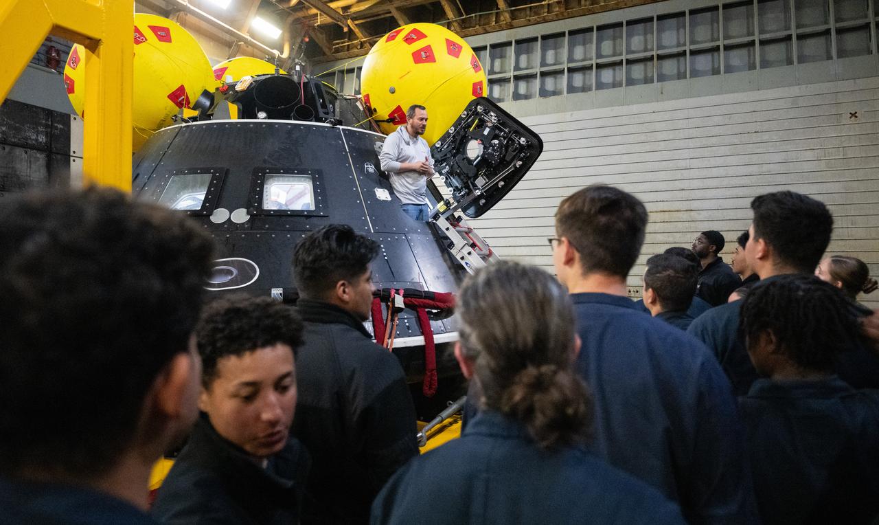 Bert Kallio, lead mechanical engineer for the Crew Module Test Article (CMTA) talks to sailors from USS Somerset as they have an opportunity to view the CMTA during Underway Recovery Test-12 onboard USS Somerset off the coast of California, Saturday, March 29, 2025. During the test, NASA and Department of Defense teams are practicing to ensure recovery procedures are validated as NASA plans to send the Artemis II astronauts around the Moon and splashdown in the Pacific Ocean.  Photo Credit: (NASA/Joel Kowsky)