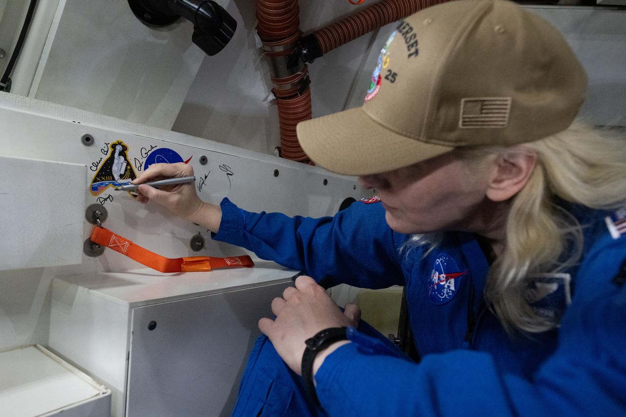 NASA astronaut Deniz Burnham signs an interior panel of the Crew Module Test Article (CMTA) during Underway Recovery Test-12 onboard USS Somerset off the coast of California, Saturday, March 29, 2025. During the test, NASA and Department of Defense teams are practicing to ensure recovery procedures are validated as NASA plans to send the Artemis II astronauts around the Moon and splashdown in the Pacific Ocean.  Photo Credit: (NASA/Joel Kowsky)