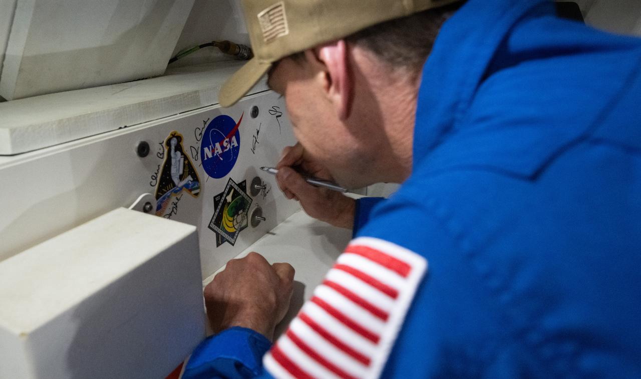 NASA astronaut Stan Love signs an interior panel of the Crew Module Test Article (CMTA) during Underway Recovery Test-12 onboard USS Somerset off the coast of California, Saturday, March 29, 2025. During the test, NASA and Department of Defense teams are practicing to ensure recovery procedures are validated as NASA plans to send the Artemis II astronauts around the Moon and splashdown in the Pacific Ocean.  Photo Credit: (NASA/Joel Kowsky)