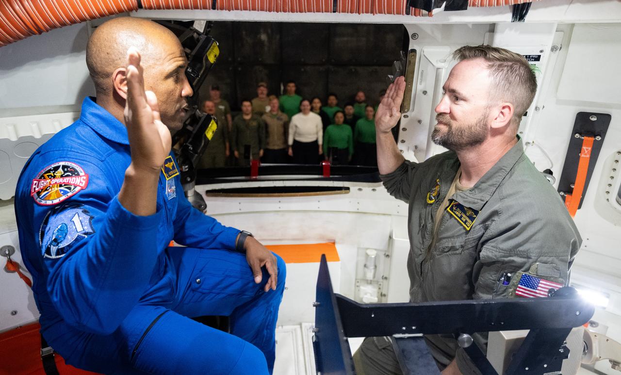 NASA astronaut U.S. Navy Capt. Victor Glover provides the oath of re-enlistment to Chief Naval Aircrewman Helicopter Sean Sondergaard in the Crew Module Test Article (CMTA) during Underway Recovery Test-12 onboard USS Somerset off the coast of California, Saturday, March 29, 2025. During the test, NASA and Department of Defense teams are practicing to ensure recovery procedures are validated as NASA plans to send the Artemis II astronauts around the Moon and splashdown in the Pacific Ocean.  Photo Credit: (NASA/Joel Kowsky)
