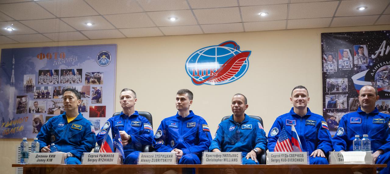 Expedition 73 crewmembers NASA astronaut Jonny Kim, left, and Roscosmos cosmonauts Sergey Ryzhikov and Alexey Zubritskiy and backup crewmembers Chris Williams of NASA, Sergey Kud-Skverchkov, and Sergey Mikaev of Roscosmos are seen in quarantine, behind glass, during a press conference, Monday, April 7, 2025 a the Cosmonaut Hotel in Baikonur, Kazakhstan. Kim, Ryzhikov, Zubritskiy are scheduled to launch aboard their Soyuz MS-27 spacecraft on April 8. Photo Credit: (NASA/Joel Kowsky)