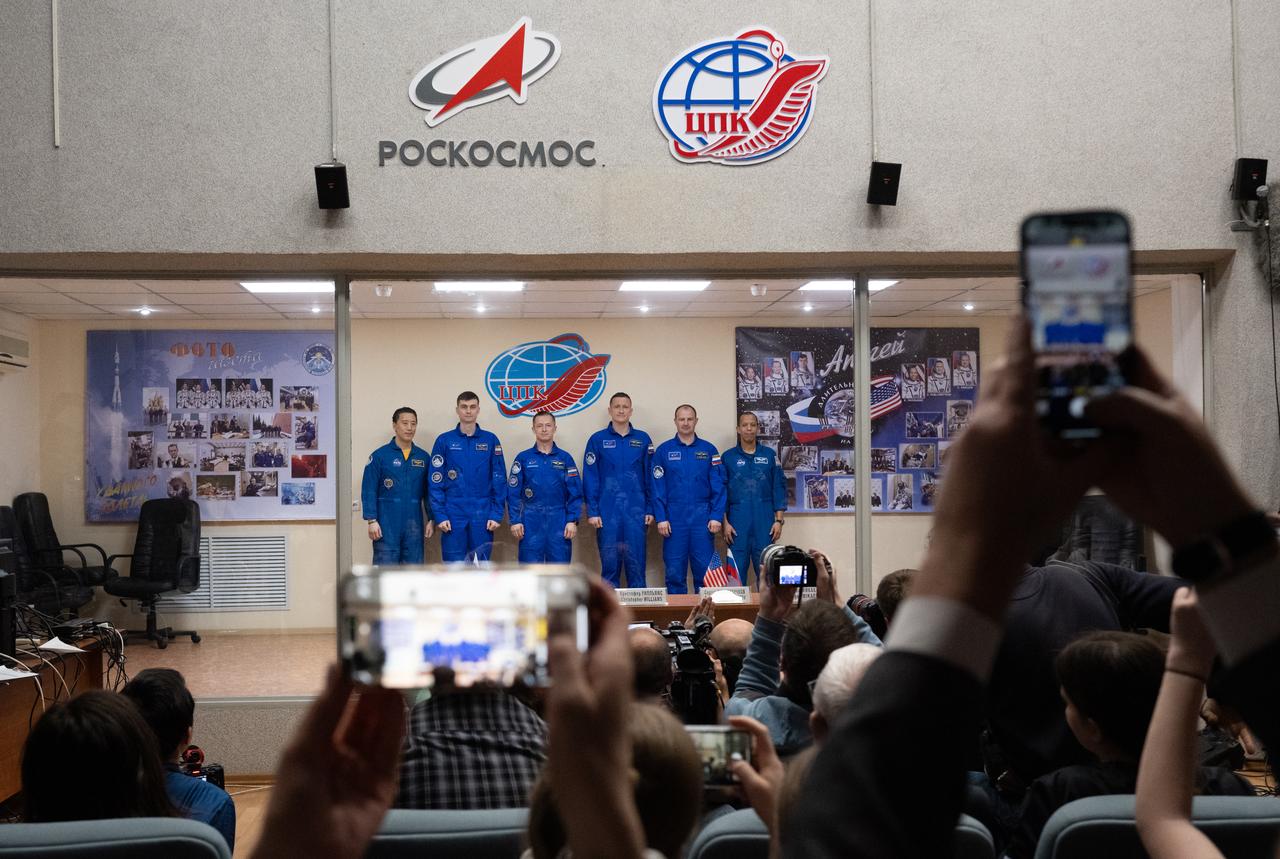 Expedition 73 crewmembers NASA astronaut Jonny Kim, left, and Roscosmos cosmonauts Alexey Zubritskiy and Sergey Ryzhikov and backup crewmembers Sergey Kud-Skverchkov, and Sergey Mikaev of Roscosmos, Chris Williams of NASA, are seen in quarantine, behind glass, as they pose for a picture at the conclusion of a press conference, Monday, April 7, 2025 a the Cosmonaut Hotel in Baikonur, Kazakhstan. Kim, Ryzhikov, Zubritskiy are scheduled to launch aboard their Soyuz MS-27 spacecraft on April 8. Photo Credit: (NASA/Joel Kowsky)