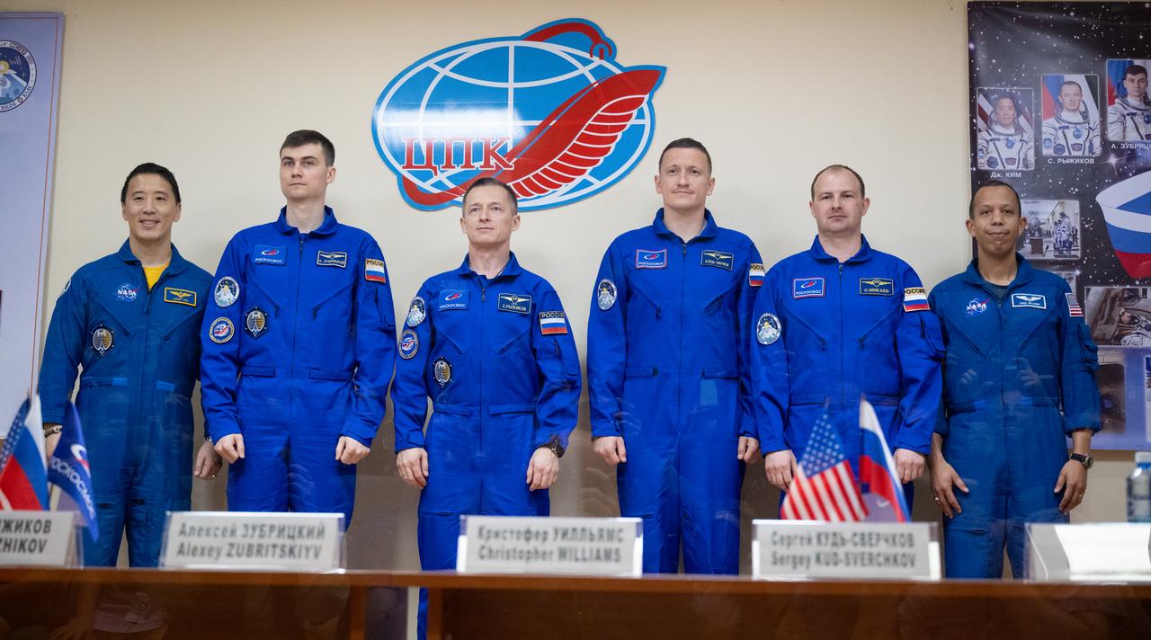 Expedition 73 crewmembers NASA astronaut Jonny Kim, left, and Roscosmos cosmonauts Alexey Zubritskiy and Sergey Ryzhikov and backup crewmembers Sergey Kud-Skverchkov, and Sergey Mikaev of Roscosmos, Chris Williams of NASA, are seen in quarantine, behind glass, as they pose for a picture at the conclusion of a press conference, Monday, April 7, 2025 a the Cosmonaut Hotel in Baikonur, Kazakhstan. Kim, Ryzhikov, Zubritskiy are scheduled to launch aboard their Soyuz MS-27 spacecraft on April 8. Photo Credit: (NASA/Joel Kowsky)