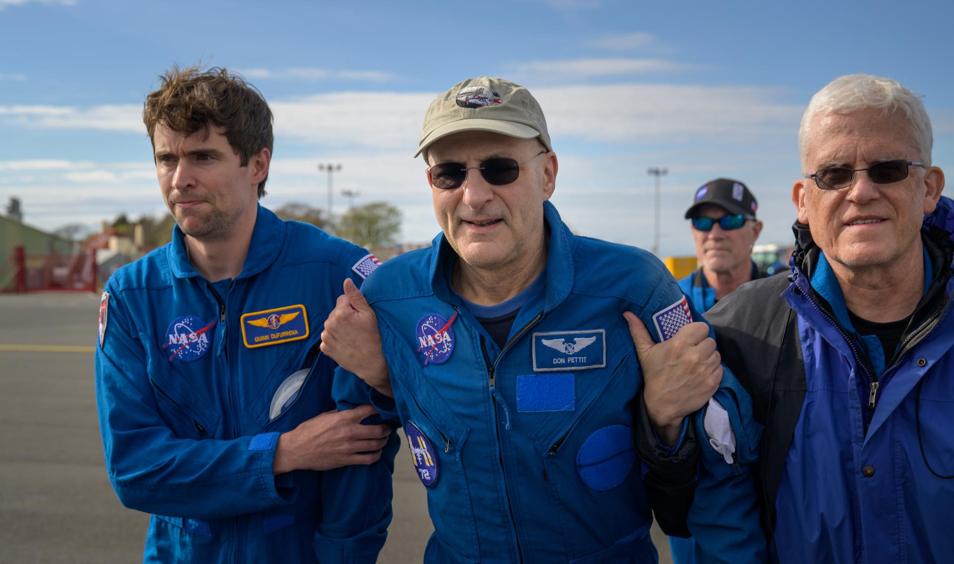 nhq202504200050 (April 20, 2025) --- NASA astronaut Don Pettit, center, walks and smiles, while supported, as part of standard post-landing procedures, by NASA Flight Surgeons Quinn Dufurrena, left, Rainer Effenhauser, right, and Richard Scheuring, background, during a brief layover in Prestwick, Scotland during his return flight to Houston from Karaganda, Kazakhstan, Sunday, April 20, 2025. Pettit, along with Roscosmos cosmonauts Alexey Ovchinin, and Ivan Vagner, returned to Earth earlier in the day after logging 220 days in space as members of Expeditions 71 and 72 aboard the International Space Station.