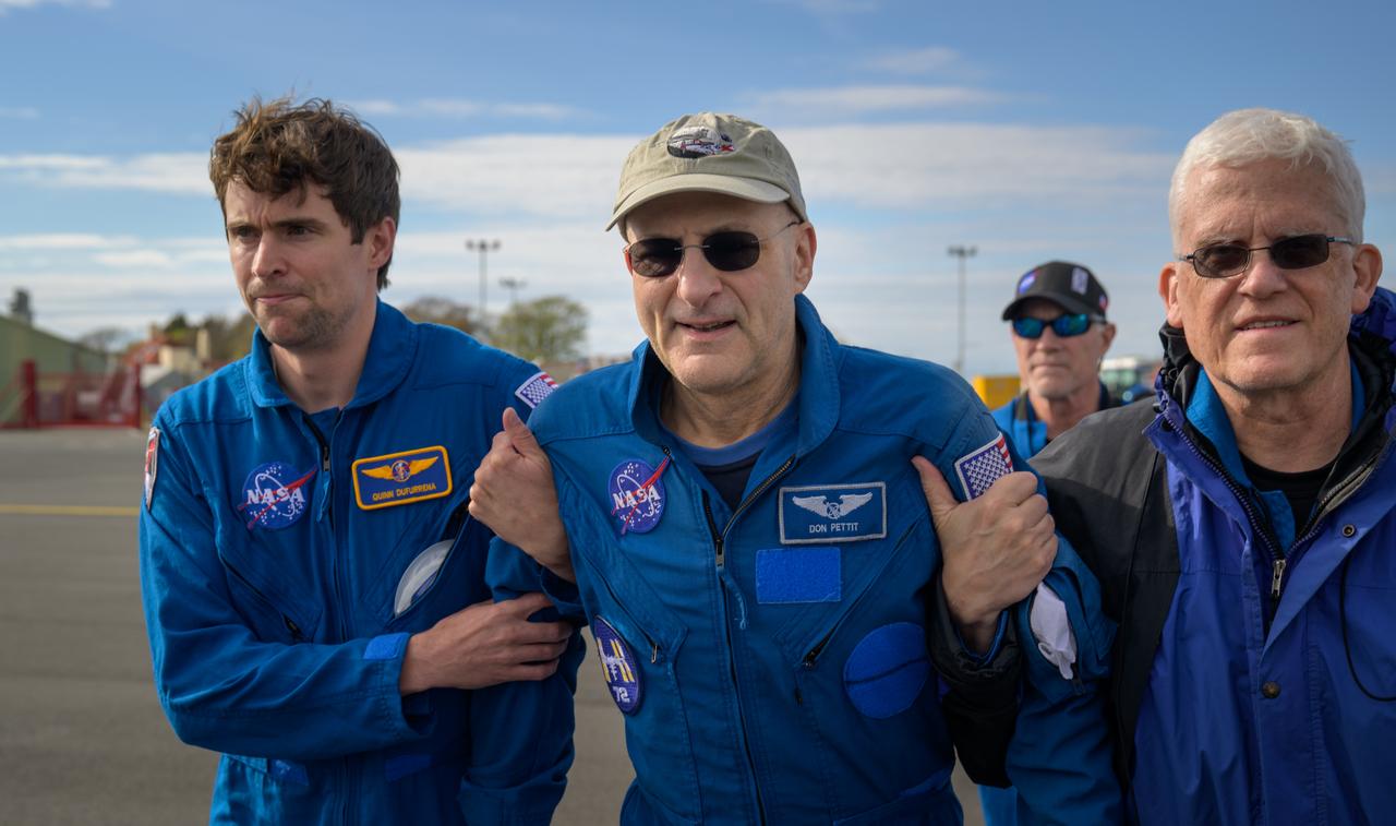 NASA astronaut Don Pettit, center, walks and smiles, while supported by NASA Flight Surgeons Quinn Dufurrena, left, Rainer Effenhauser, right, and Richard Scheuring, background, during a brief layover in Prestwick, Scotland during his return flight to Houston from Karaganda, Kazakhstan, Sunday, April 20, 2025. Pettit, along with Roscosmos cosmonauts Alexey Ovchinin, and Ivan Vagner, returned to Earth earlier in the day after logging 220 days in space as members of Expeditions 71 and 72 aboard the International Space Station. Photo Credit: (NASA/Bill Ingalls)
