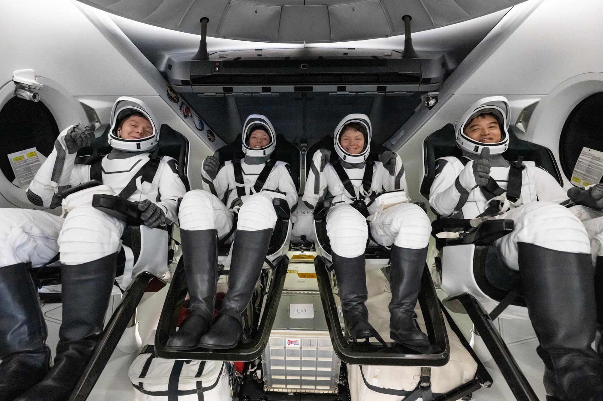 Image shows four astronauts in white and black suits posing for a photo inside the SpaceX crew capsule. From left, Roscosmos cosmonaut Kirill Peskov, NASA astronauts Nicole Ayers, Anne McClain, and JAXA (Japan Aerospace Exploration Agency) astronaut Takuya Onishi. Photo credit: NASA/Keegan Barber