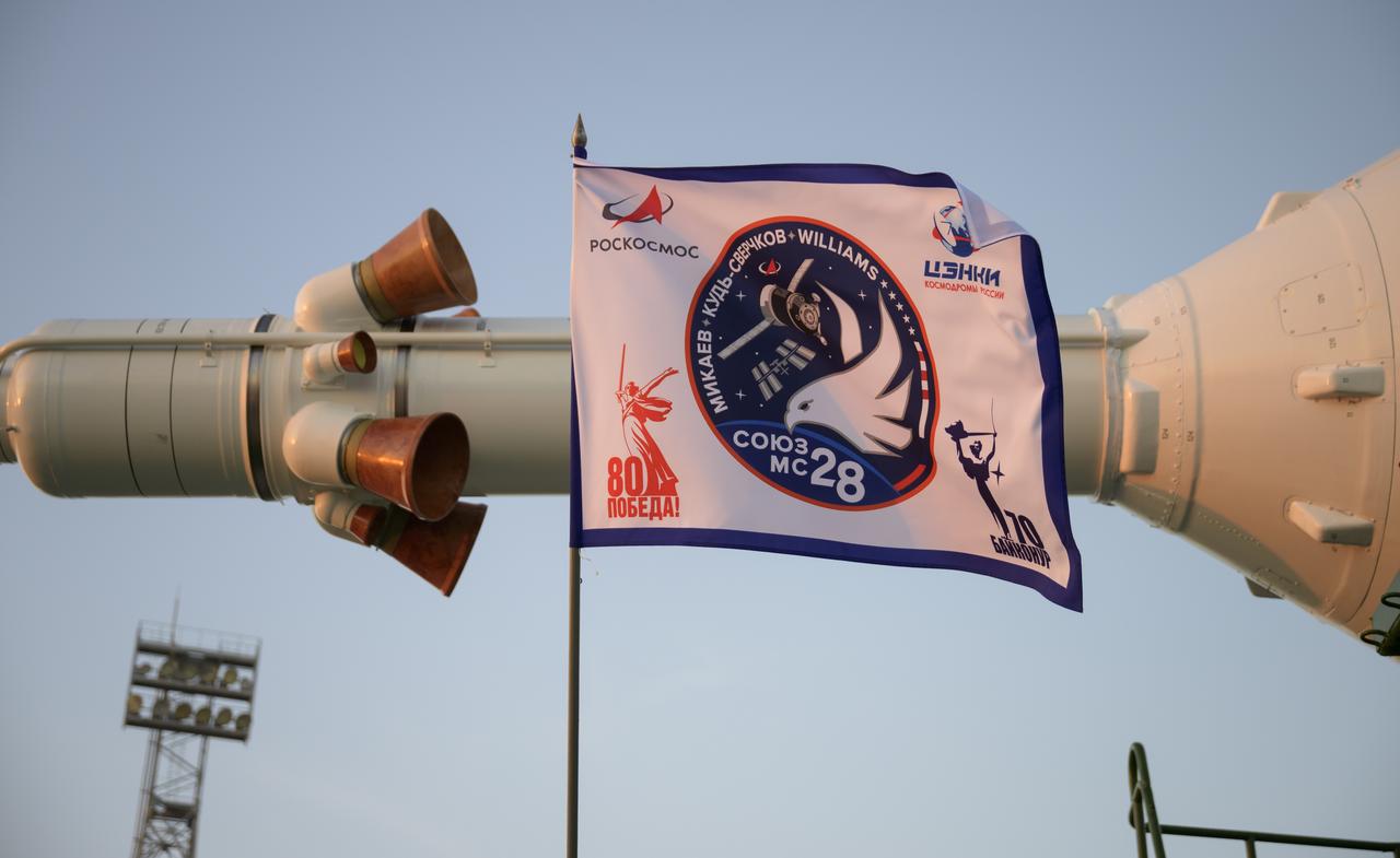 A flag attached to the train rolling out the  Soyuz rocket to the launch pad is seen, Monday, Nov. 24, 2025, at Site 31 of the Baikonur Cosmodrome in Kazakhstan. Expedition 74 crewmembers: NASA astronaut Chris Williams, Roscosmos cosmonauts Sergey Kud-Sverchkov and Sergey Mikaev are scheduled to launch aboard their Soyuz MS-28 spacecraft on November 27. Photo Credit: (NASA/Bill Ingalls)