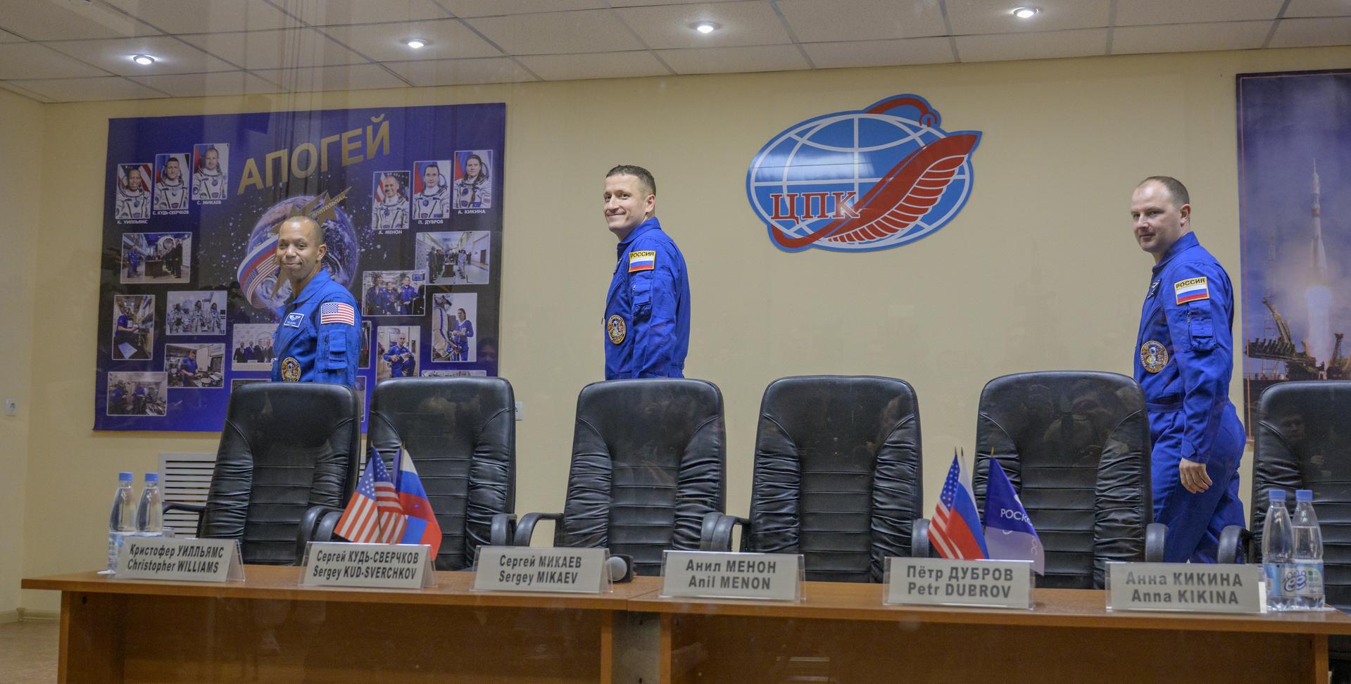 NASA astronaut Chris Williams, left, and Roscosmos cosmonauts Sergey Kud-Sverchkov, and Sergei Mikaev, right, are seen in quarantine, behind glass, as they arrive at a press conference, Wednesday, Nov. 26, 2025 at the Cosmonaut Hotel in Baikonur, Kazakhstan. Expedition 74 crewmembers: NASA astronaut Chris Williams, Roscosmos cosmonauts Sergey Kud-Sverchkov and Sergei Mikaev, are scheduled to launch aboard their Soyuz MS-28 spacecraft on November 27. Photo Credit: (NASA/Bill Ingalls)
