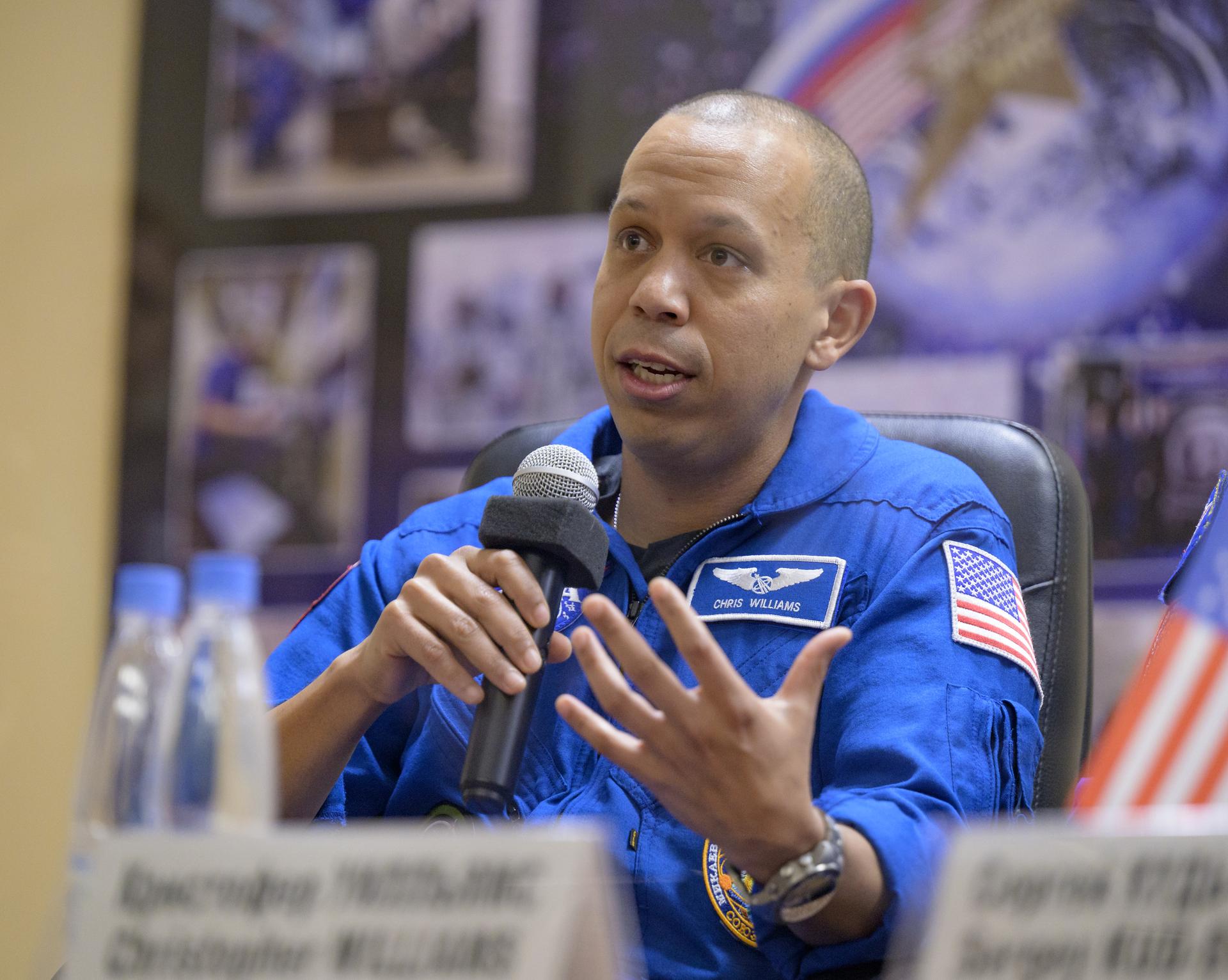 NASA astronaut Chris Williams is seen in quarantine, behind glass, during a press conference, Wednesday, Nov. 26, 2025 at the Cosmonaut Hotel in Baikonur, Kazakhstan. Expedition 74 crewmembers: Williams, Roscosmos cosmonauts Sergey Kud-Sverchkov and Sergei Mikaev, are scheduled to launch aboard their Soyuz MS-28 spacecraft on November 27. Photo Credit: (NASA/Bill Ingalls)