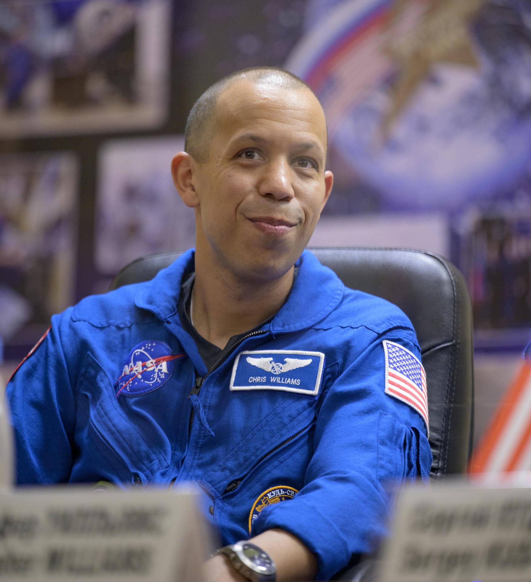 NASA astronaut Chris Williams is seen in quarantine, behind glass, during a press conference, Wednesday, Nov. 26, 2025 at the Cosmonaut Hotel in Baikonur, Kazakhstan. Expedition 74 crewmembers: Williams, Roscosmos cosmonauts Sergey Kud-Sverchkov and Sergei Mikaev, are scheduled to launch aboard their Soyuz MS-28 spacecraft on November 27. Photo Credit: (NASA/Bill Ingalls)