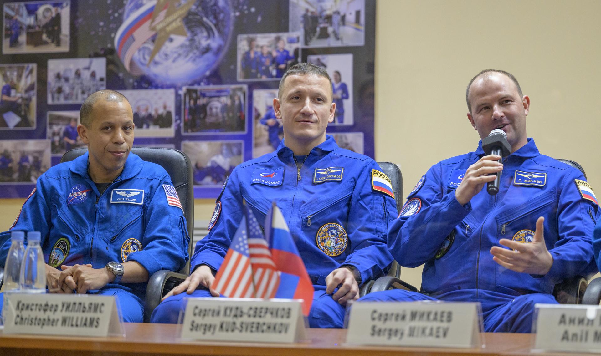 NASA astronaut Chris Williams, left, and Roscosmos cosmonauts Sergey Kud-Sverchkov, and Sergei Mikaev, right, are seen in quarantine, behind glass, during a press conference, Wednesday, Nov. 26, 2025 at the Cosmonaut Hotel in Baikonur, Kazakhstan. Expedition 74 crewmembers: NASA astronaut Chris Williams, Roscosmos cosmonauts Sergey Kud-Sverchkov and Sergei Mikaev, are scheduled to launch aboard their Soyuz MS-28 spacecraft on November 27. Photo Credit: (NASA/Bill Ingalls)