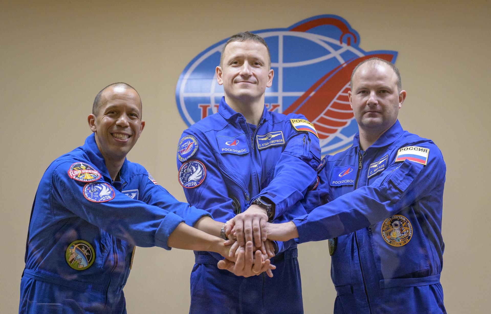 NASA astronaut Chris Williams, left, and Roscosmos cosmonauts Sergey Kud-Sverchkov, and Sergei Mikaev, right, are seen in quarantine, behind glass, at the conclusion of a press conference, Wednesday, Nov. 26, 2025 at the Cosmonaut Hotel in Baikonur, Kazakhstan. Expedition 74 crewmembers: NASA astronaut Chris Williams, Roscosmos cosmonauts Sergey Kud-Sverchkov and Sergei Mikaev, are scheduled to launch aboard their Soyuz MS-28 spacecraft on November 27. Photo Credit: (NASA/Bill Ingalls)