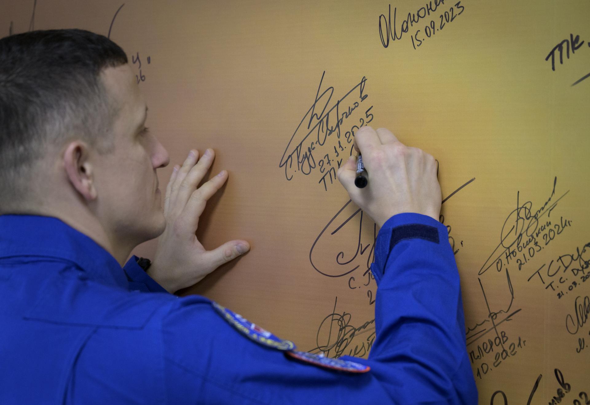 Roscosmos cosmonaut Sergey Kud-Sverchkov signs a mural at the Cosmonaut Hotel prior to departing for suit-up and launch on a Soyuz rocket with fellow crewmates NASA astronaut Chris Williams, and Roscosmos cosmonaut Sergei Mikaev, Thursday, Nov. 27, 2025, in Baikonur, Kazakhstan. The launch will send Williams, Kud-Sverchkov and Mikaev, on a mission to the International Space Station. Photo Credit: (NASA/Bill Ingalls)