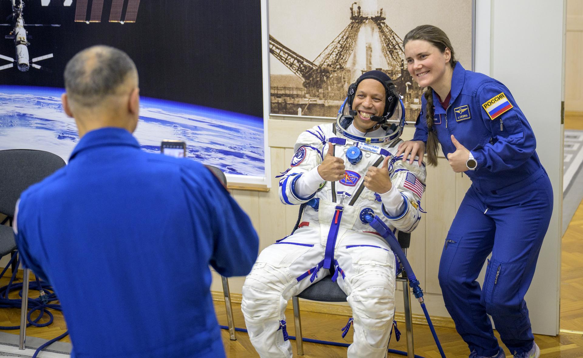 NASA astronaut Chris Williams has his photo made with Expedition 74 backup crew member Anna Kikina of Roscosmos, by Expedition 74 backup crew member Anil Menon of NASA, as he waits to have his Russian Sokol suit pressure checked ahead of his launch on the Soyuz Rocket to the International Space Station with fellow crewmembers, Roscosmos cosmonauts Sergey Kud-Sverchkov, and Sergei Mikaev, Thursday, Nov. 27, 2025 in Baikonur, Kazakhstan. Photo Credit: (NASA/Bill Ingalls)