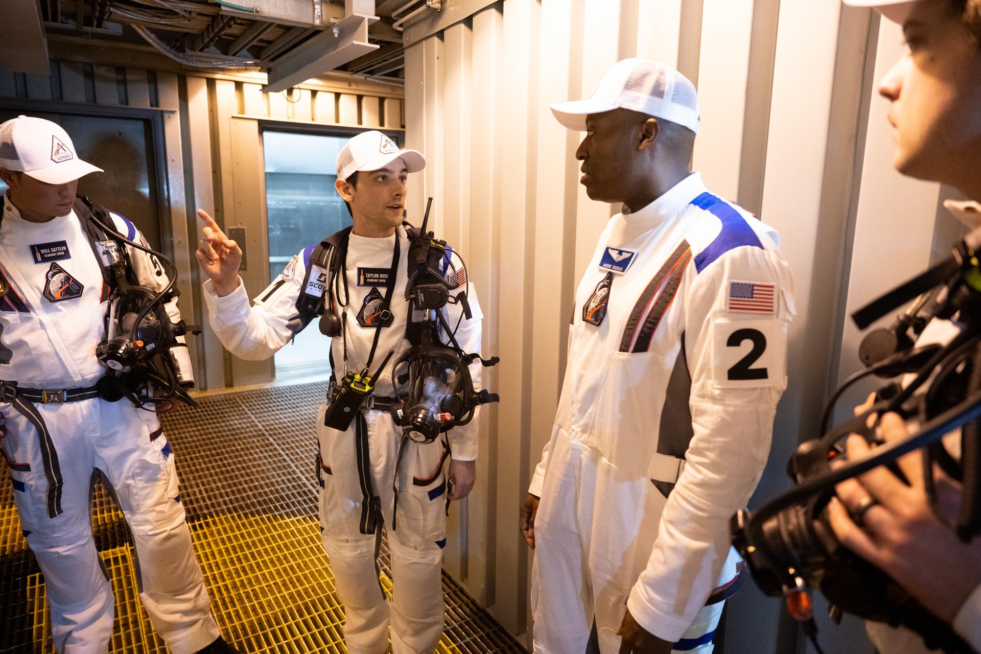 Closeout Crew lead Taylor Hose, second from left, talks with NASA astronaut Andre Douglas, second from right as he and closeout crewmembers Will Sattler, left, and Christian Warriner prepare for the arrival of Artemis II crewmembers NASA astronauts Reid Wiseman, commander; Victor Glover, pilot; Christina Koch, mission specialist; and CSA (Canadian Space Agency) astronaut Jeremy Hansen, mission specialist; at the 275-foot level of the mobile launcher as they prepare to board their Orion spacecraft atop NASA’s Space Launch System rocket during the Artemis II countdown demonstration test, Saturday, Dec. 20, 2025, inside the Vehicle Assembly Building at NASA’s Kennedy Space Center in Florida. For this operation, the Artemis II crew and launch teams are simulating the launch day timeline including suit-up, walkout, and spacecraft ingress and egress.  Through the Artemis campaign, NASA will send astronauts to explore the Moon for scientific discovery, economic benefits, and to build the foundation for the first crewed missions to Mars, for the benefit of all. Photo Credit: (NASA/Joel Kowsky)
