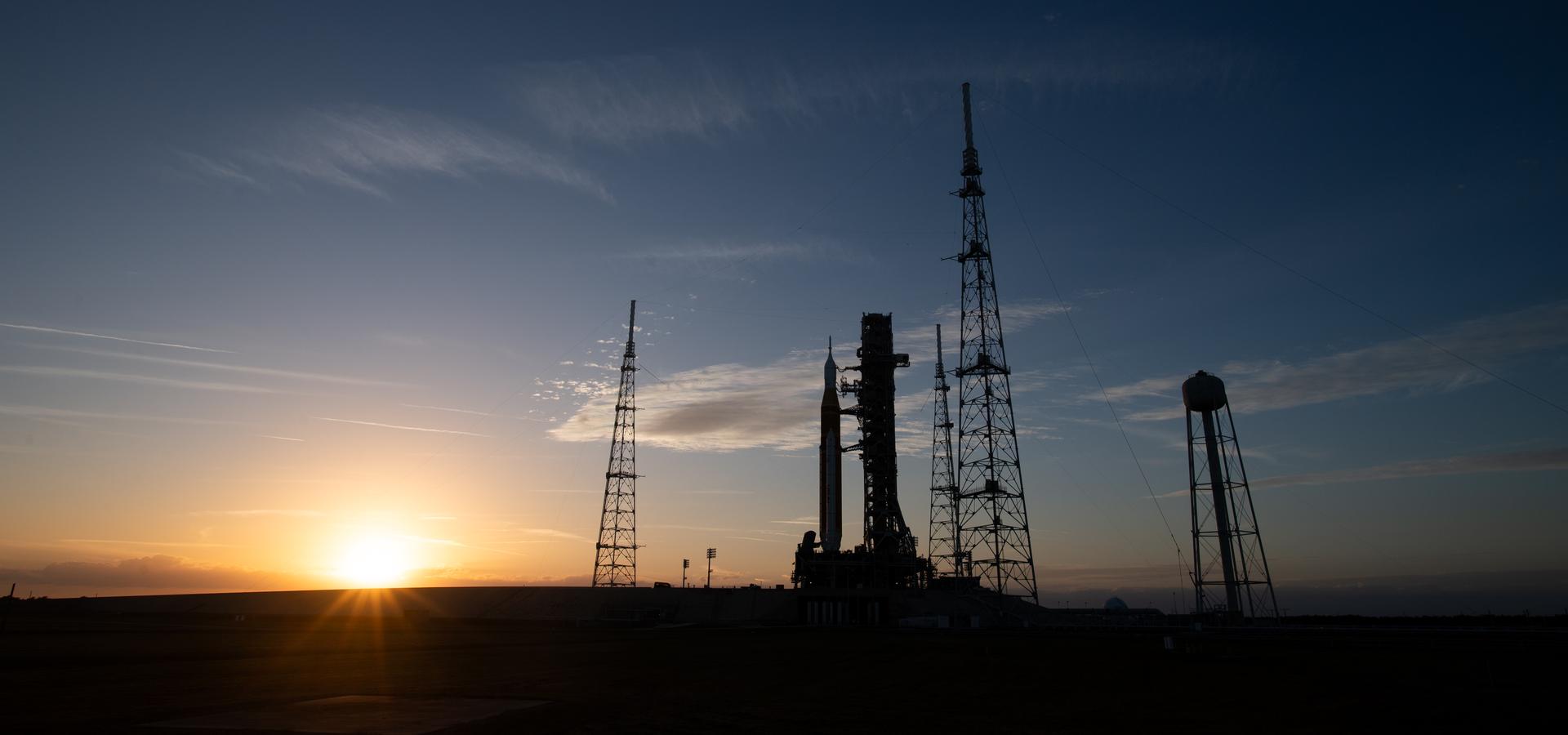 NASA’s Artemis II Space Launch System (SLS) rocket and Orion spacecraft are seen as the Sun sets after arriving at Launch Complex 39B, Saturday, Jan. 17, 2026, at NASA’s Kennedy Space Center in Florida. In the coming days, engineers will prepare for the wet dress rehearsal, a two-day test that simulates launch day. The Artemis II test flight will take Commander Reid Wiseman, Pilot Victor Glover, and Mission Specialist Christina Koch from NASA, and Mission Specialist Jeremy Hansen from the CSA (Canadian Space Agency), around the Moon and back to Earth no later than April 2026. Photo Credit: (NASA/Joel Kowsky)