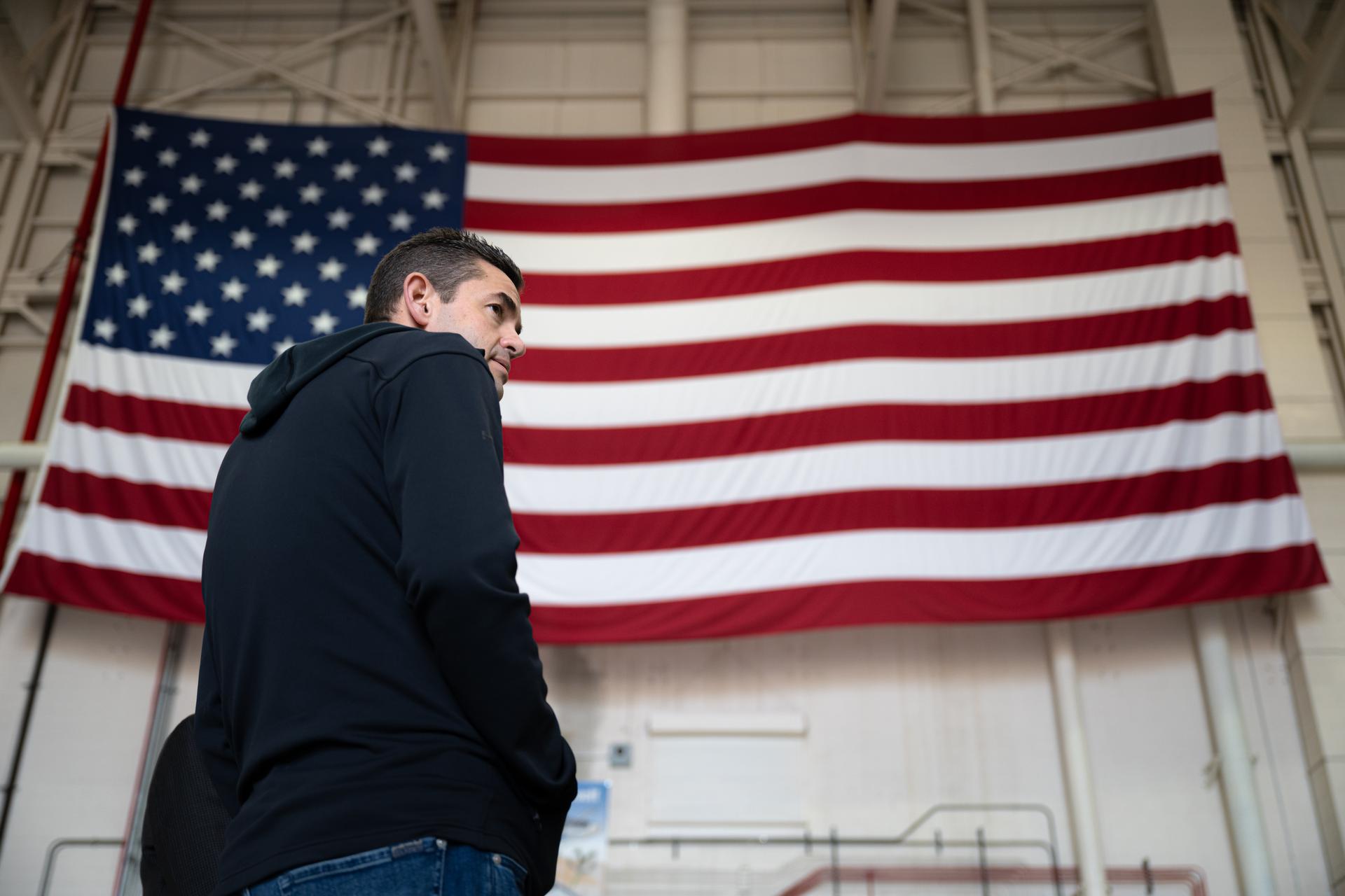 NASA Administrator Jared Isaacman is seen in front of an American flag in a hangar, Sunday, Jan. 25, 2026, at NASA’s Armstrong Flight Research Center at Edwards Air Force Base in California. Armstrong marks the ninth stop in Isaacman’s roadshow to visit NASA facilities and engage directly with the agency’s workforce. Photo Credit: (NASA/John Kraus)