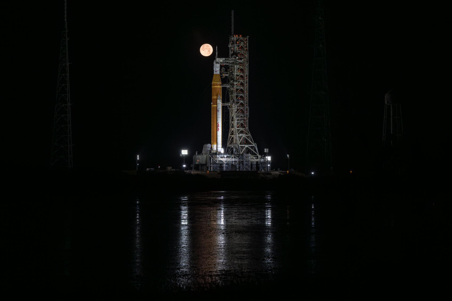 The full Moon is seen behind NASA’s Artemis II Space Launch System (SLS) rocket and Orion spacecraft, standing atop a mobile launcher at Launch Complex 39B, Sunday, Feb. 1, 2026, at NASA’s Kennedy Space Center in Florida. NASA’s Artemis II test flight will take Commander Reid Wiseman, Pilot Victor Glover, and Mission Specialist Christina Koch from NASA, and Mission Specialist Jeremy Hansen from the CSA (Canadian Space Agency), around the Moon and back to Earth no later than April 2026. Photo Credit: (NASA/John Kraus)