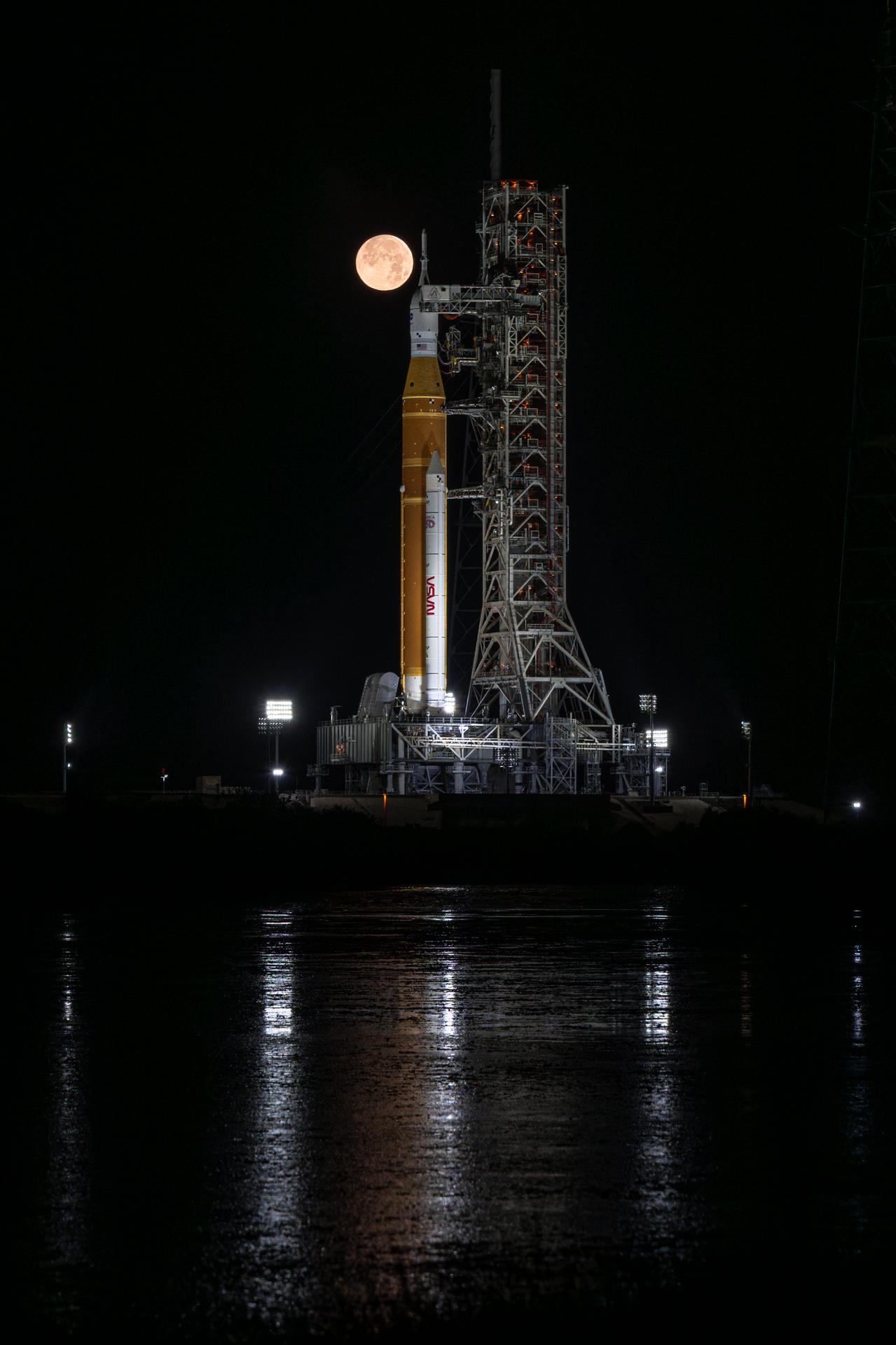 The full Moon is seen behind NASA’s Artemis II Space Launch System (SLS) rocket and Orion spacecraft, standing atop a mobile launcher at Launch Complex 39B, Sunday, Feb. 1, 2026, at NASA’s Kennedy Space Center in Florida. NASA’s Artemis II test flight will take Commander Reid Wiseman, Pilot Victor Glover, and Mission Specialist Christina Koch from NASA, and Mission Specialist Jeremy Hansen from the CSA (Canadian Space Agency), around the Moon and back to Earth no later than April 2026. Photo Credit: (NASA/John Kraus)