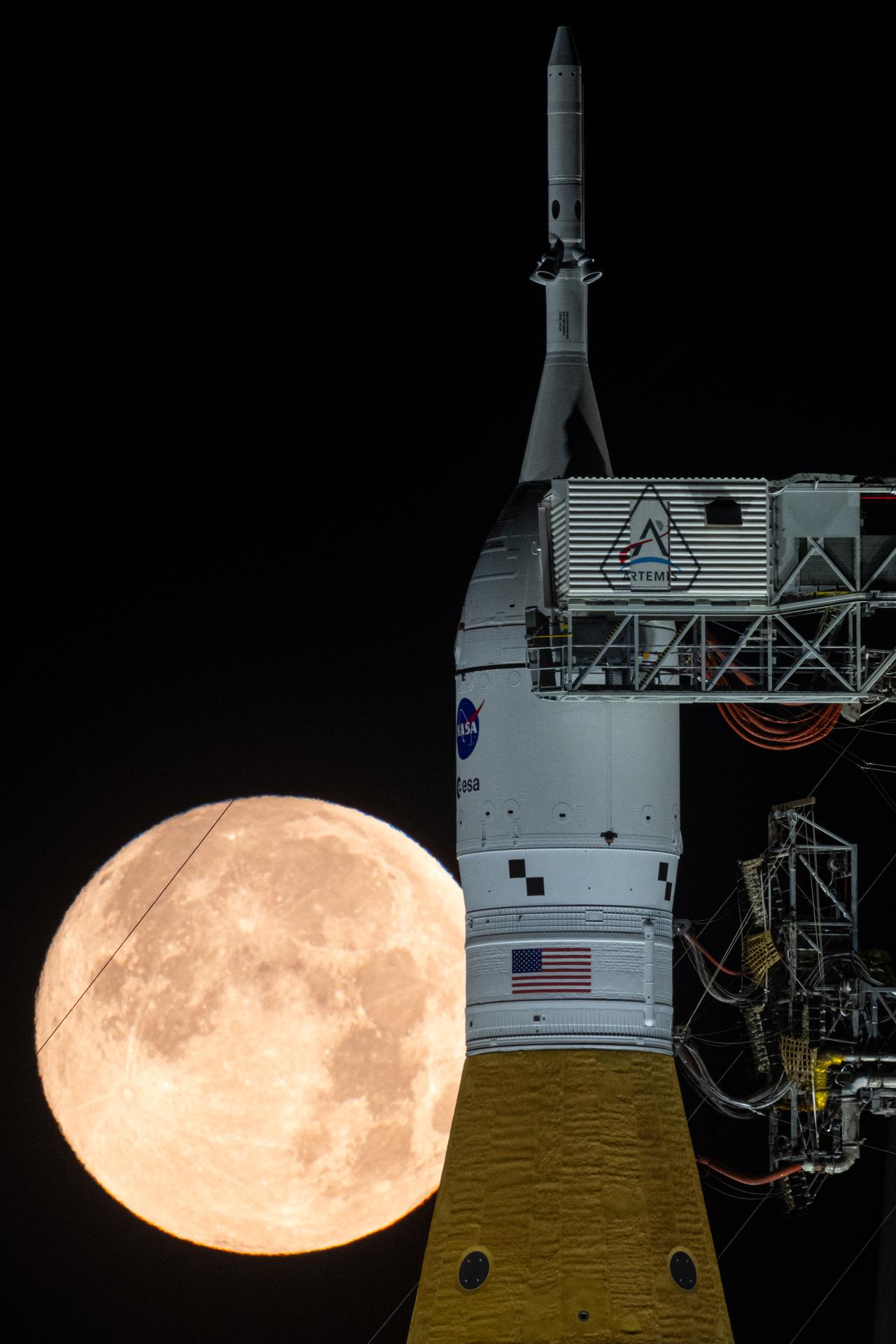 The full Moon is seen behind NASA’s Artemis II Space Launch System (SLS) rocket and Orion spacecraft, standing atop a mobile launcher at Launch Complex 39B, Sunday, Feb. 1, 2026, at NASA’s Kennedy Space Center in Florida. NASA’s Artemis II test flight will take Commander Reid Wiseman, Pilot Victor Glover, and Mission Specialist Christina Koch from NASA, and Mission Specialist Jeremy Hansen from the CSA (Canadian Space Agency), around the Moon and back to Earth no later than April 2026. Photo Credit: (NASA/John Kraus)