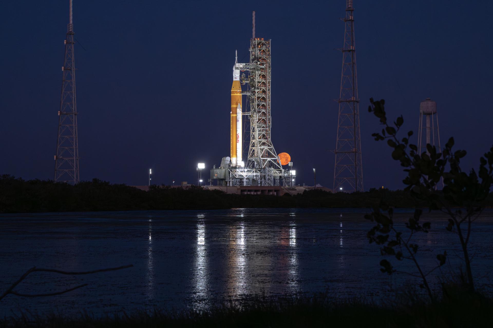 The full Moon is seen behind NASA’s Artemis II Space Launch System (SLS) rocket and Orion spacecraft, standing atop a mobile launcher at Launch Complex 39B, Sunday, Feb. 1, 2026, at NASA’s Kennedy Space Center in Florida. NASA’s Artemis II test flight will take Commander Reid Wiseman, Pilot Victor Glover, and Mission Specialist Christina Koch from NASA, and Mission Specialist Jeremy Hansen from the CSA (Canadian Space Agency), around the Moon and back to Earth no later than April 2026. Photo Credit: (NASA/John Kraus)