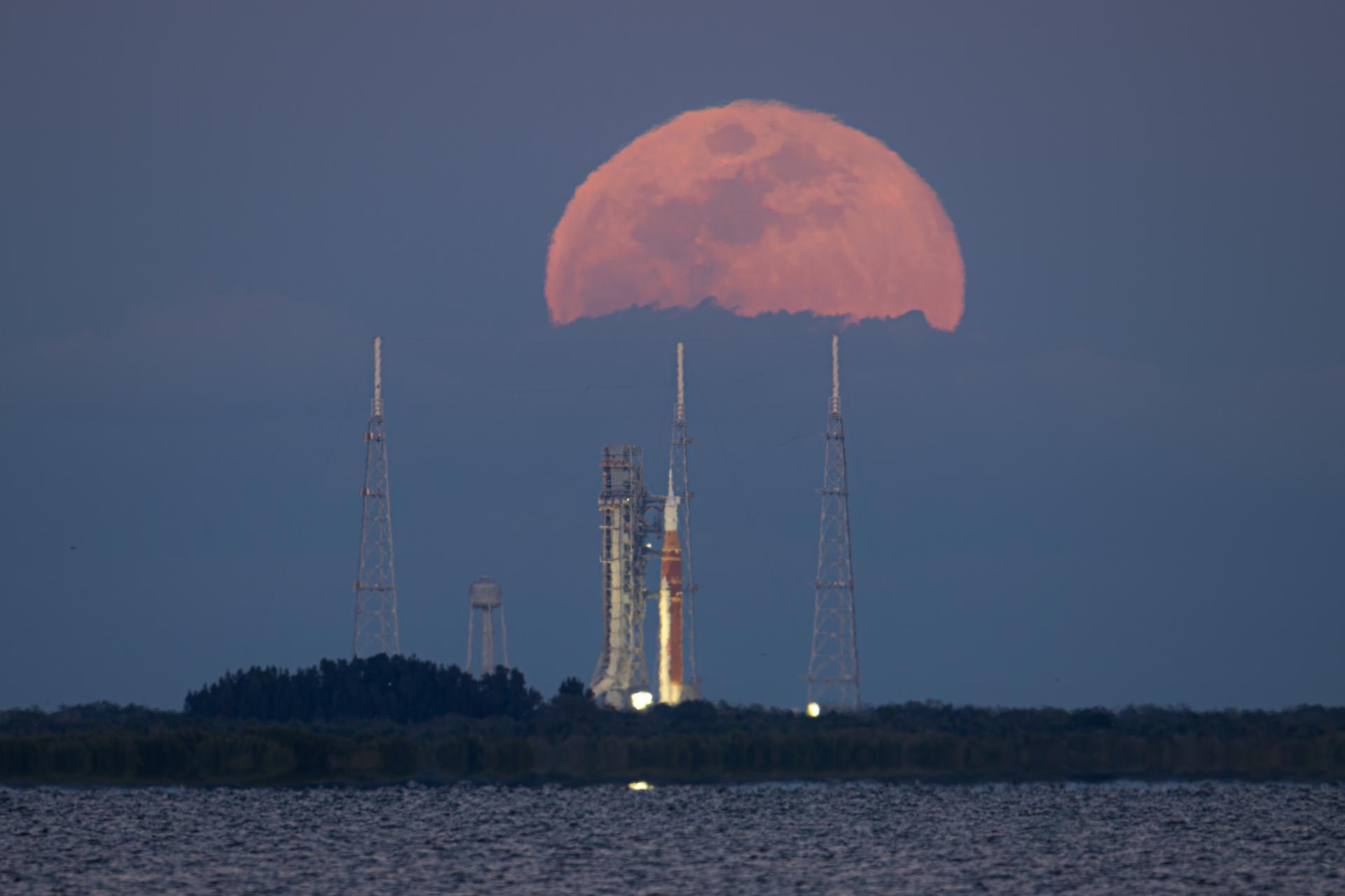 The full Moon rises behind NASA’s Artemis II Space Launch System (SLS) rocket and Orion spacecraft, standing atop a mobile launcher at Launch Complex 39B, Sunday, Feb. 1, 2026, at NASA’s Kennedy Space Center, as seen from Titusville, Fla. NASA’s Artemis II test flight will take Commander Reid Wiseman, Pilot Victor Glover, and Mission Specialist Christina Koch from NASA, and Mission Specialist Jeremy Hansen from the CSA (Canadian Space Agency), around the Moon and back to Earth no later than April 2026. Photo Credit: (NASA/John Kraus)