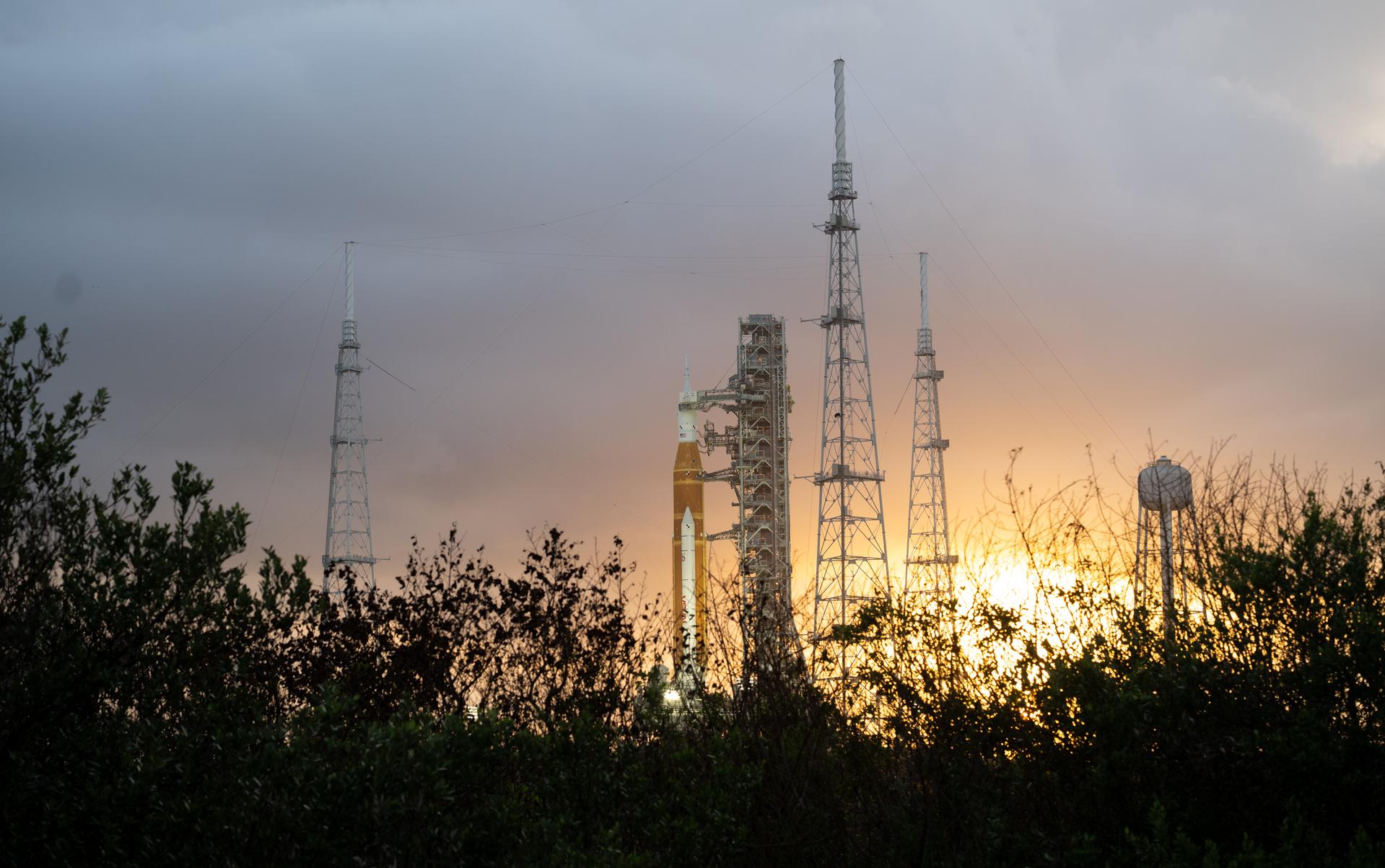 NASA’s Artemis II Space Launch System (SLS) rocket and Orion spacecraft are seen at sunset atop a mobile launcher at Launch Complex 39B, Monday, March 30, 2026, as preparations continue for launch at NASA’s Kennedy Space Center in Florida. NASA’s Artemis II test flight will take Commander Reid Wiseman, Pilot Victor Glover, and Mission Specialist Christina Koch from NASA, and Mission Specialist Jeremy Hansen from the CSA (Canadian Space Agency), around the Moon and back to Earth no later than no later than April 2026. Photo Credit: (NASA/Joel Kowsky)