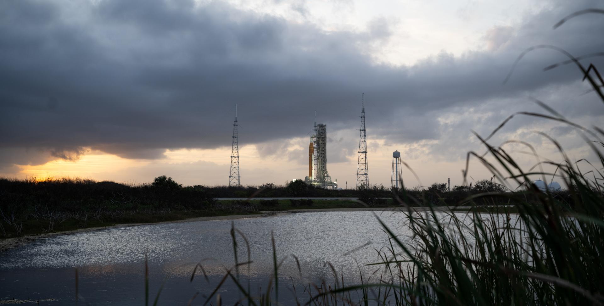 NASA’s Artemis II Space Launch System (SLS) rocket and Orion spacecraft are seen at sunset atop a mobile launcher at Launch Complex 39B, Monday, March 30, 2026, as preparations continue for launch at NASA’s Kennedy Space Center in Florida. NASA’s Artemis II test flight will take Commander Reid Wiseman, Pilot Victor Glover, and Mission Specialist Christina Koch from NASA, and Mission Specialist Jeremy Hansen from the CSA (Canadian Space Agency), around the Moon and back to Earth no later than no later than April 2026. Photo Credit: (NASA/Joel Kowsky)