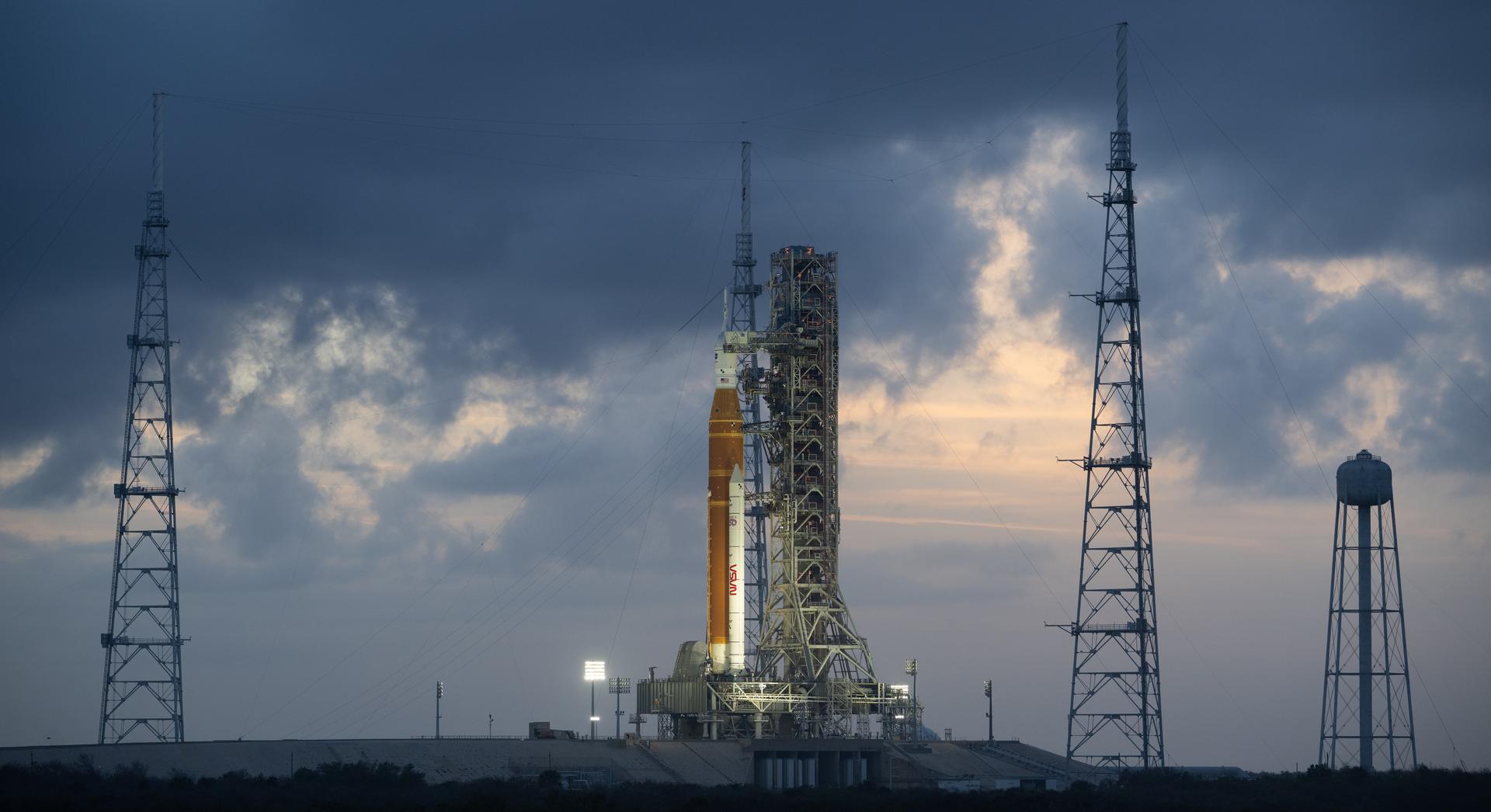 NASA’s Artemis II Space Launch System (SLS) rocket and Orion spacecraft are seen at sunset atop a mobile launcher at Launch Complex 39B, Monday, March 30, 2026, as preparations continue for launch at NASA’s Kennedy Space Center in Florida. NASA’s Artemis II test flight will take Commander Reid Wiseman, Pilot Victor Glover, and Mission Specialist Christina Koch from NASA, and Mission Specialist Jeremy Hansen from the CSA (Canadian Space Agency), around the Moon and back to Earth no later than no later than April 2026. Photo Credit: (NASA/Joel Kowsky)
