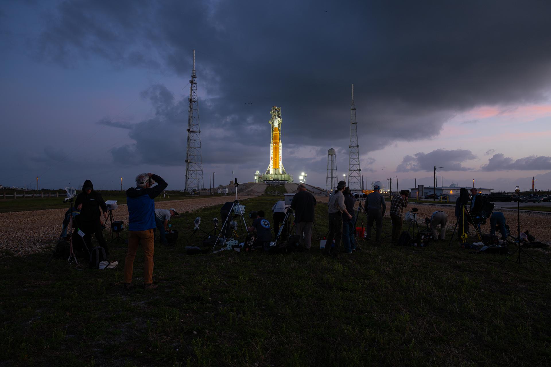 Members of the media position their remote cameras and capture photographs as NASA’s Artemis II Space Launch System (SLS) rocket and Orion spacecraft are seen standing atop a mobile launcher at Launch Complex 39B, Tuesday, March 31, 2026, at NASA’s Kennedy Space Center in Florida. NASA’s Artemis II test flight will take Commander Reid Wiseman, Pilot Victor Glover, and Mission Specialist Christina Koch from NASA, and Mission Specialist Jeremy Hansen from the CSA (Canadian Space Agency), around the Moon and back to Earth no earlier than April 1, 2026. Photo Credit: (NASA/John Kraus)