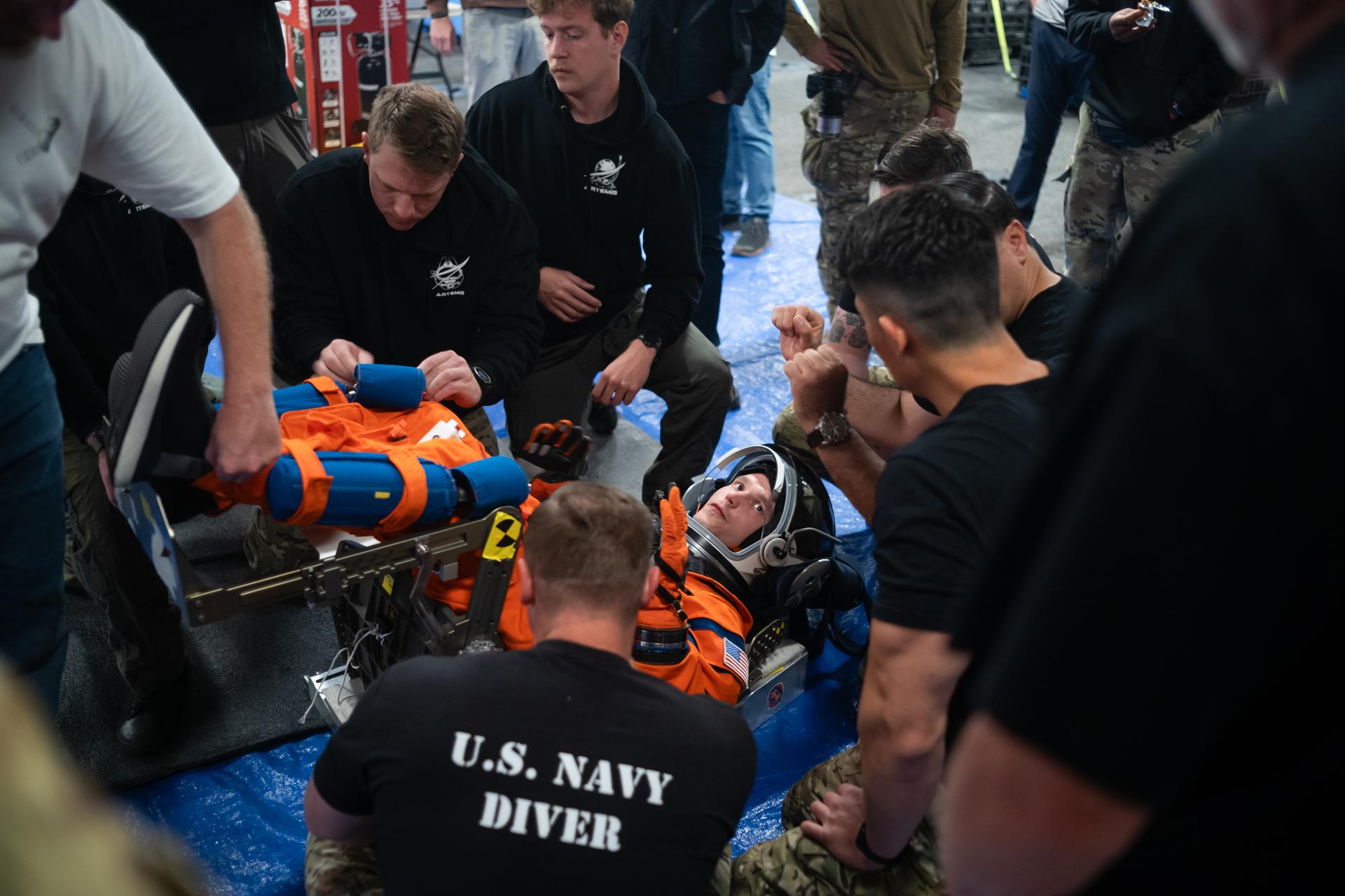 Nicholas Houghton, an Orion Crew Survival System engineer at NASA’s Johnson Space Center, wearing an Orion Crew Survival System suit, conducts familiarization training with U.S. Navy divers on doffing the suit onboard USS John P. Murtha ahead of the return of the Artemis II crewmembers to Earth, Tuesday, April 7, 2026, in the Pacific Ocean off the coast of California. NASA’s Artemis II mission is taking NASA astronauts Reid Wiseman, commander; Victor Glover, pilot; Christina Koch, mission specialist; and CSA (Canadian Space Agency) astronaut Jeremy Hansen, mission specialist on a 10-day journey around the Moon and back aboard their Orion spacecraft. Wiseman, Glover, Koch, and Hansen are scheduled to splash down off the coast of San Diego at approximately 5:07 p.m. PDT (8:07 p.m. EDT) on Friday, April 10.  Photo Credit: (NASA/Joel Kowsky)