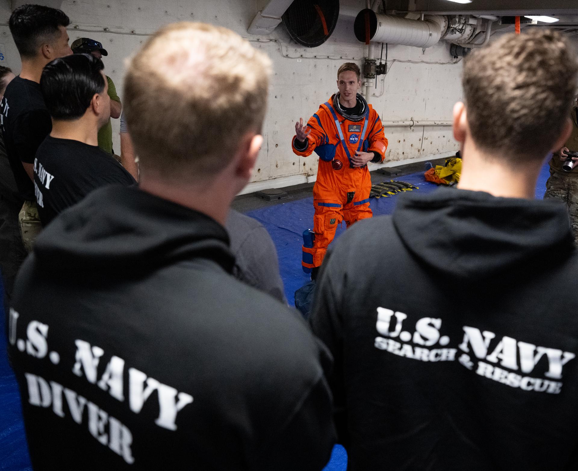 Nicholas Houghton, an Orion Crew Survival System engineer at NASA’s Johnson Space Center, wearing an Orion Crew Survival System suit, conducts familiarization training with U.S. Navy divers on doffing the suit onboard USS John P. Murtha ahead of the return of the Artemis II crewmembers to Earth, Tuesday, April 7, 2026, in the Pacific Ocean off the coast of California. NASA’s Artemis II mission is taking NASA astronauts Reid Wiseman, commander; Victor Glover, pilot; Christina Koch, mission specialist; and CSA (Canadian Space Agency) astronaut Jeremy Hansen, mission specialist on a 10-day journey around the Moon and back aboard their Orion spacecraft. Wiseman, Glover, Koch, and Hansen are scheduled to splash down off the coast of San Diego at approximately 5:07 p.m. PDT (8:07 p.m. EDT) on Friday, April 10.  Photo Credit: (NASA/Joel Kowsky)