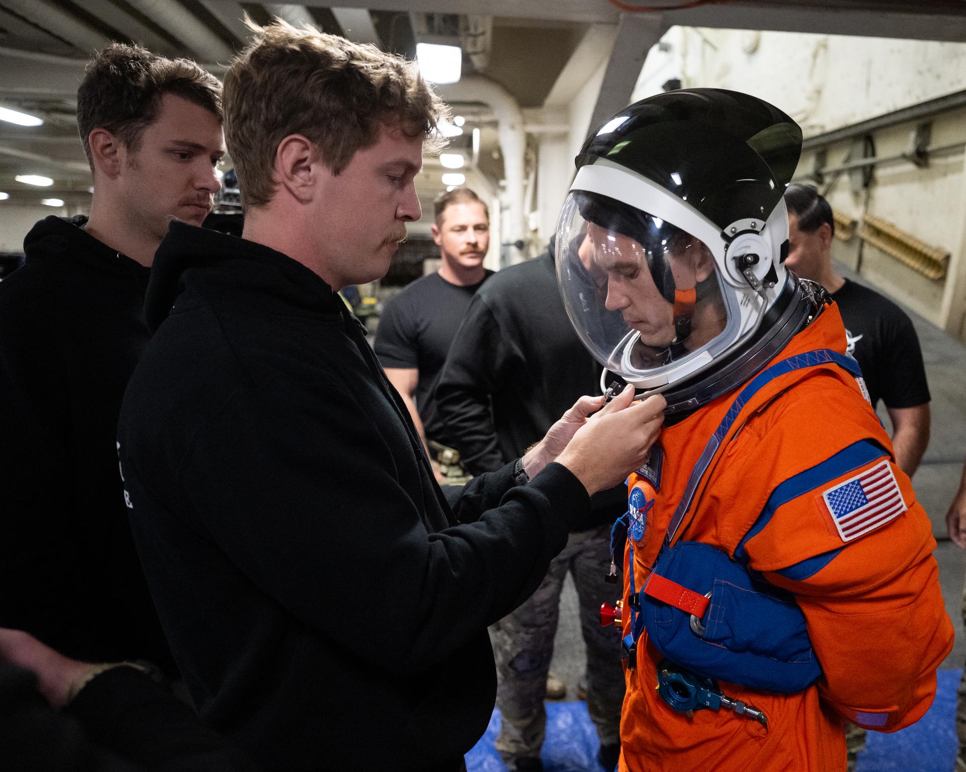 Nicholas Houghton, an Orion Crew Survival System engineer at NASA’s Johnson Space Center, wearing an Orion Crew Survival System suit, conducts familiarization training with U.S. Navy divers on doffing the suit onboard USS John P. Murtha ahead of the return of the Artemis II crewmembers to Earth, Tuesday, April 7, 2026, in the Pacific Ocean off the coast of California. NASA’s Artemis II mission is taking NASA astronauts Reid Wiseman, commander; Victor Glover, pilot; Christina Koch, mission specialist; and CSA (Canadian Space Agency) astronaut Jeremy Hansen, mission specialist on a 10-day journey around the Moon and back aboard their Orion spacecraft. Wiseman, Glover, Koch, and Hansen are scheduled to splash down off the coast of San Diego at approximately 5:07 p.m. PDT (8:07 p.m. EDT) on Friday, April 10.  Photo Credit: (NASA/Joel Kowsky)